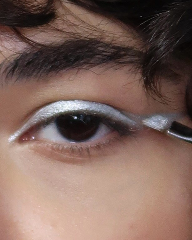 Close-up von Auge mit silber Lidschattem und Pinsel, der das Auge schminkt