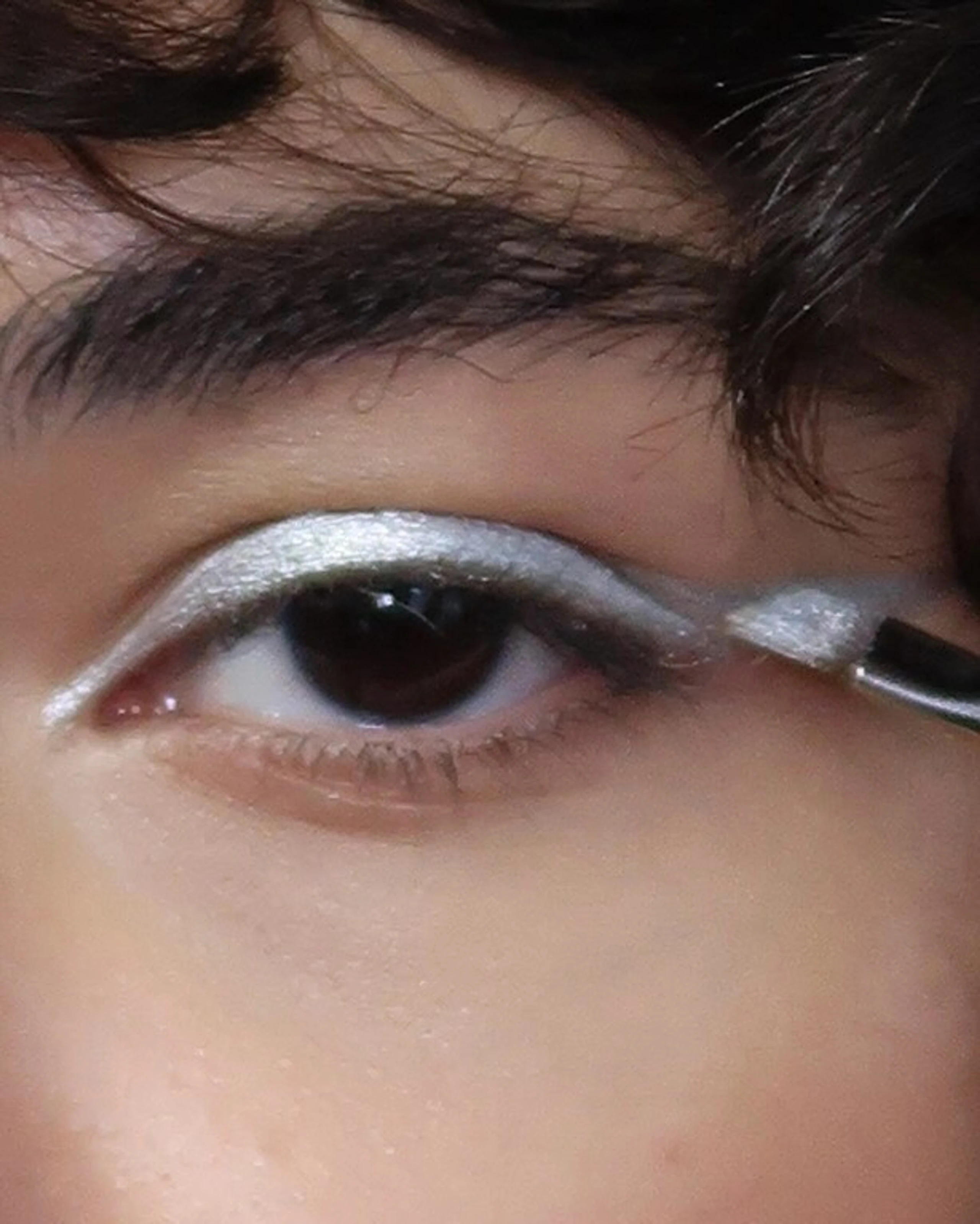 Close-up von Auge mit silber Lidschattem und Pinsel, der das Auge schminkt