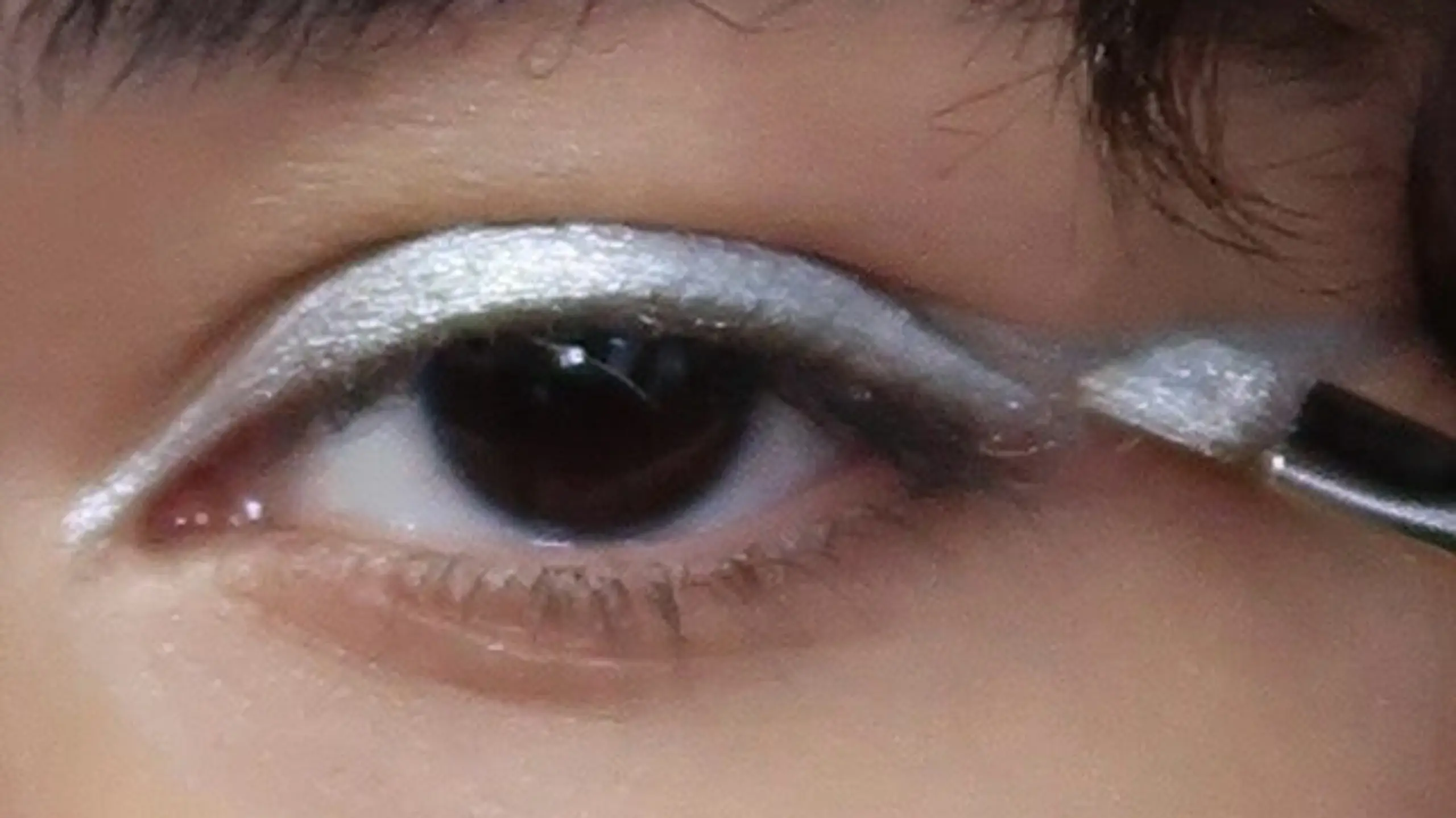 Close-up von Auge mit silber Lidschattem und Pinsel, der das Auge schminkt