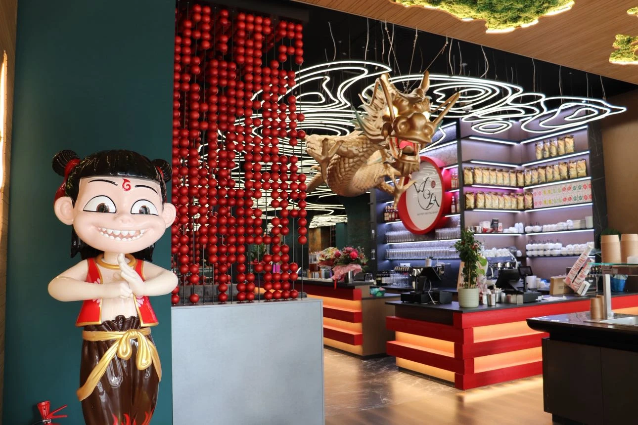 Restaurant Interieur mit Cartoon-Figur, rotem Kugelvorhang und Drachenskulptur.
