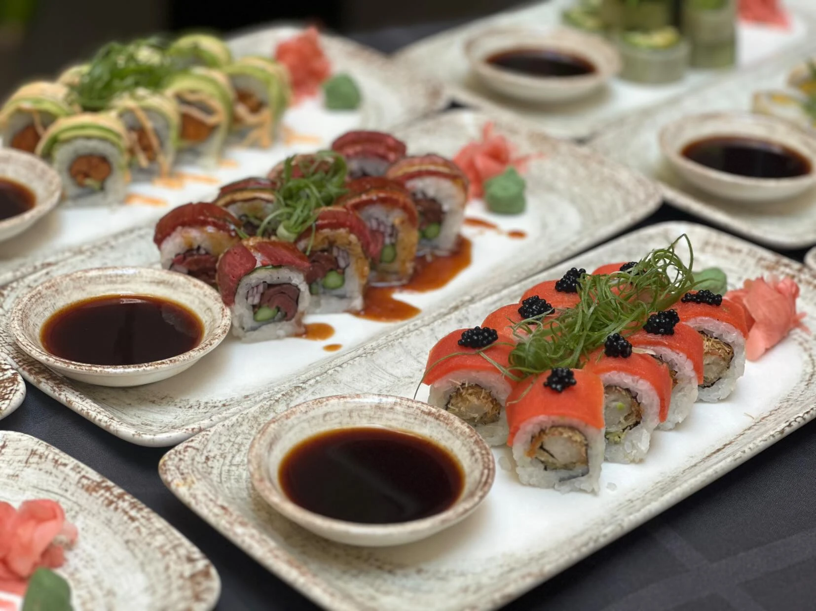 Verschiedene Sushi-Rollen auf Tellern mit Sojasauce, Wasabi und Ingwer.