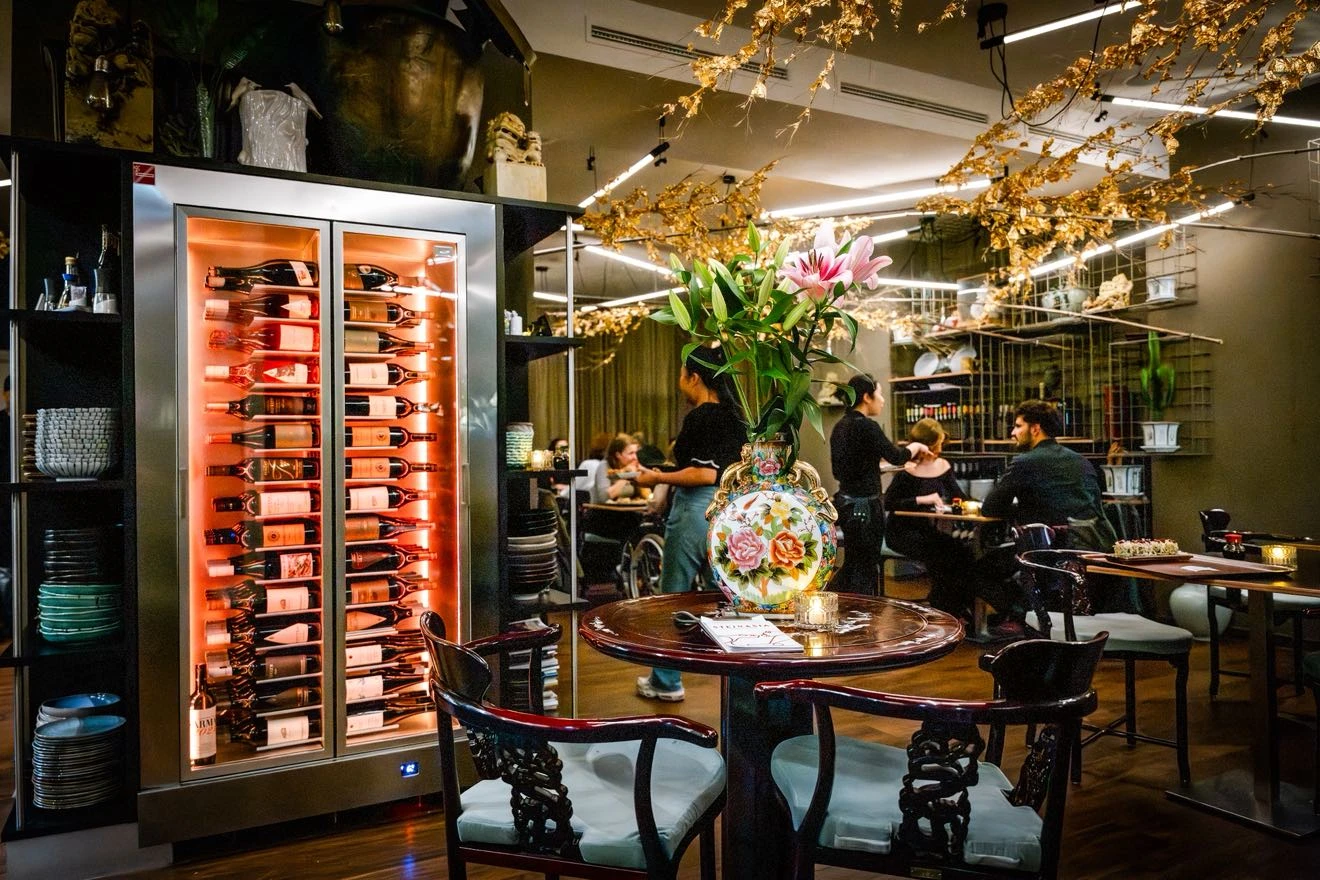 Elegantes Restaurant mit Weinkühlschrank, floralem Arrangement und Gästen.