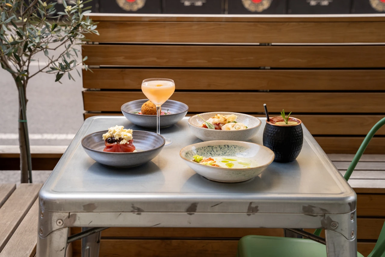 Tisch im Freien mit Cocktail, frittierter Kugel, Salaten und Getränk im schwarzen Becher.