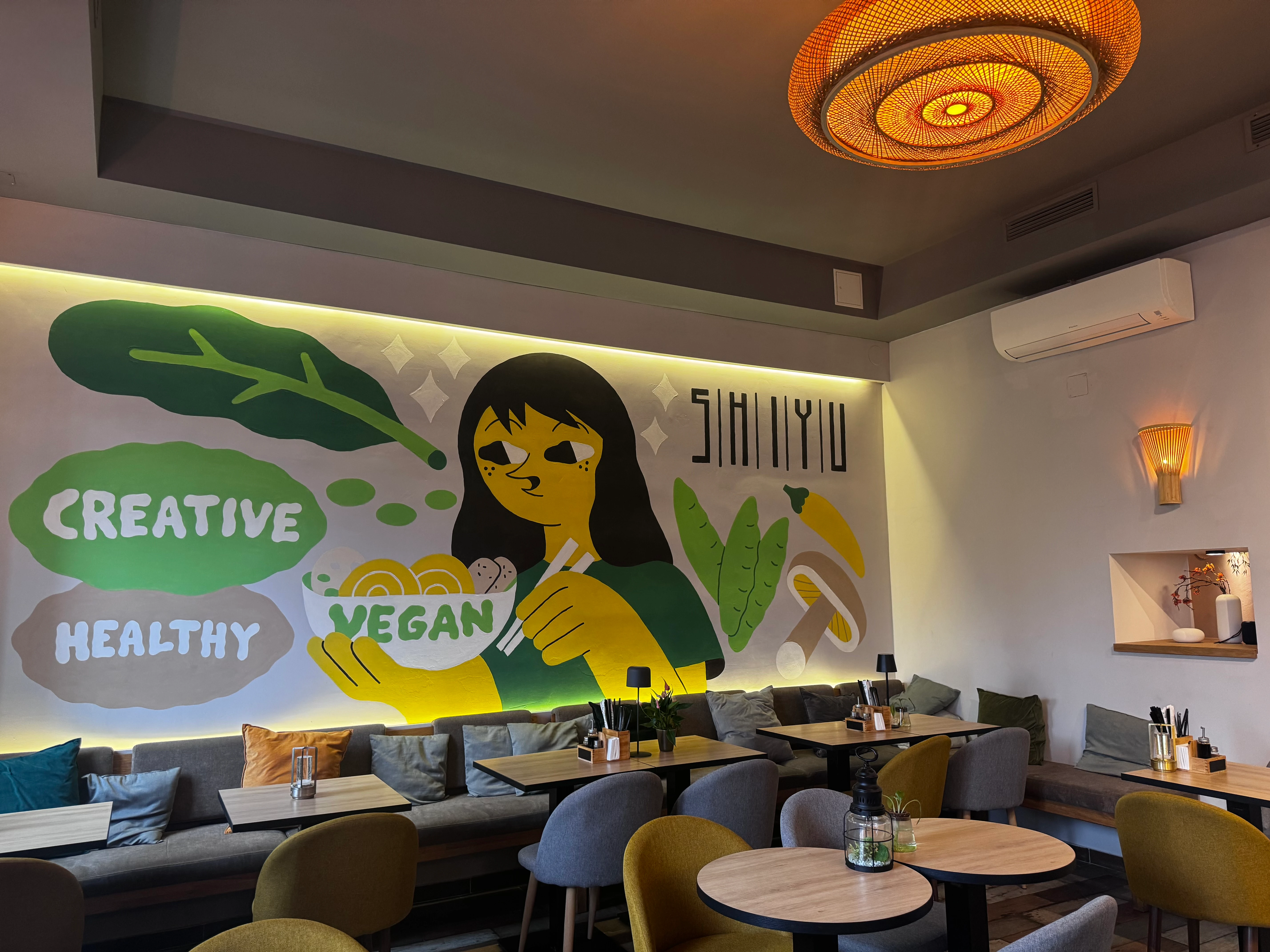 Restaurantinnenraum mit Wandgemälde einer veganen Figur. Gemütliche Sitzecken und kreatives Design für gesunde Mahlzeiten.