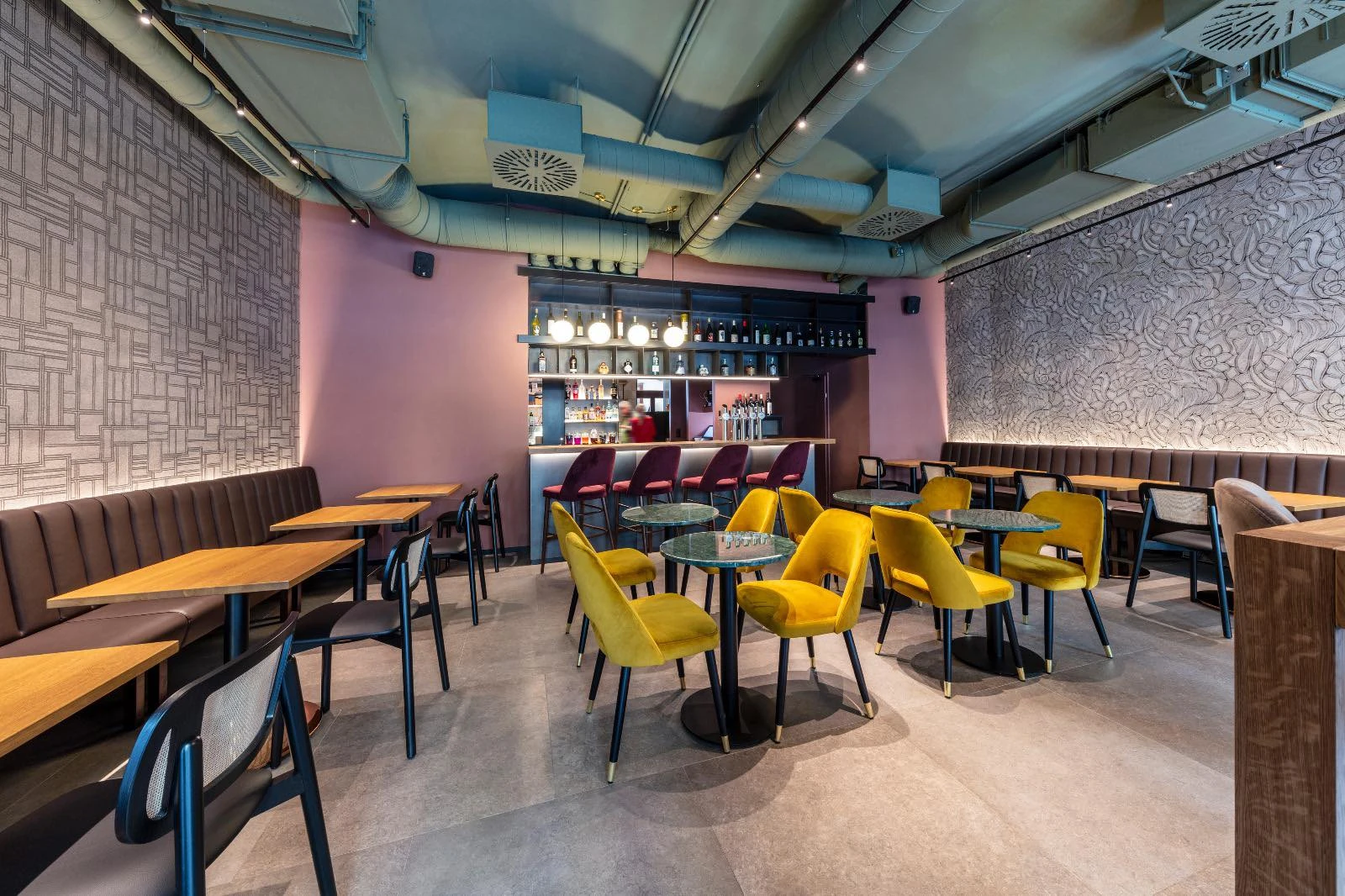 Innenansicht eines stilvollen Restaurants mit Bar, Tischen und gelben Stühlen.