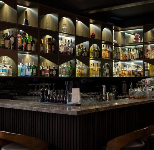 Gut sortierte Bar mit Spirituosen, Gläsern und Barutensilien in stilvollem Ambiente.