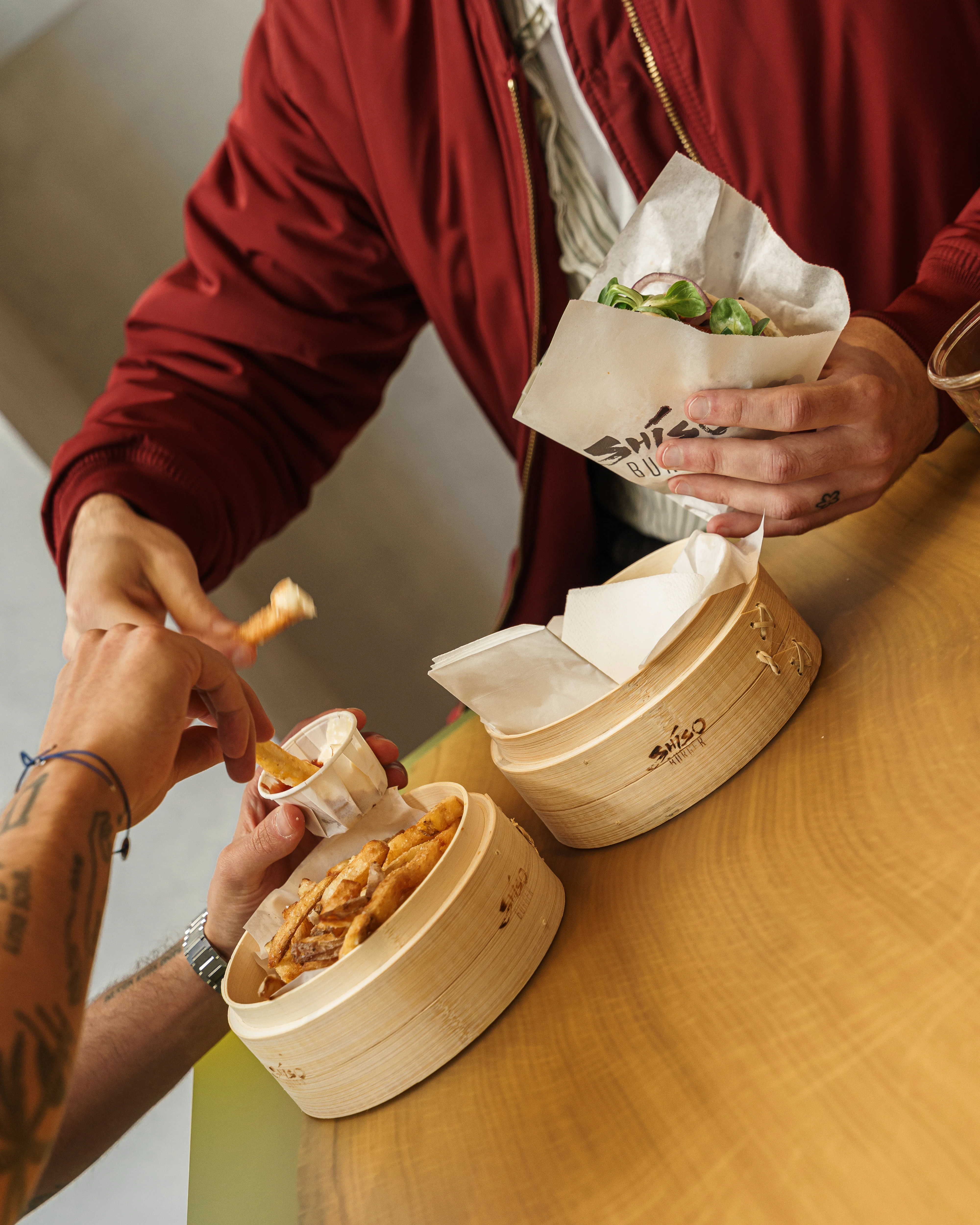 Zwei Personen teilen sich Burger und Pommes an einem Tisch.