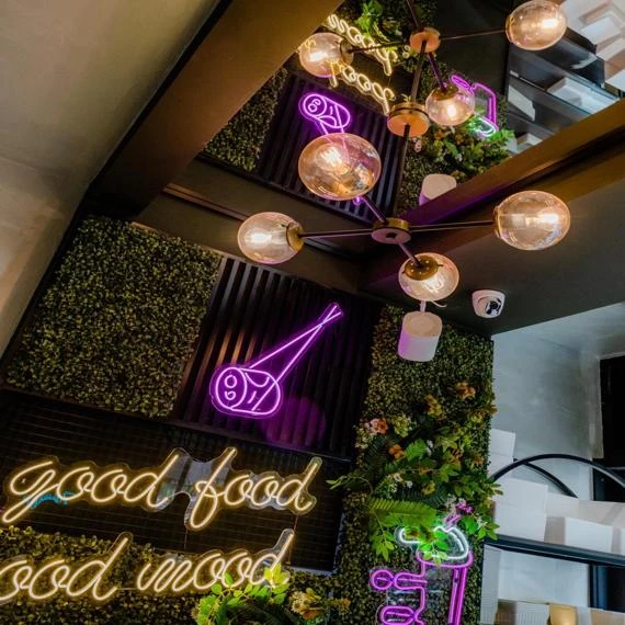 Trendiges Restaurant mit Neonzeichen, moderner Beleuchtung und grüner Wanddekoration.