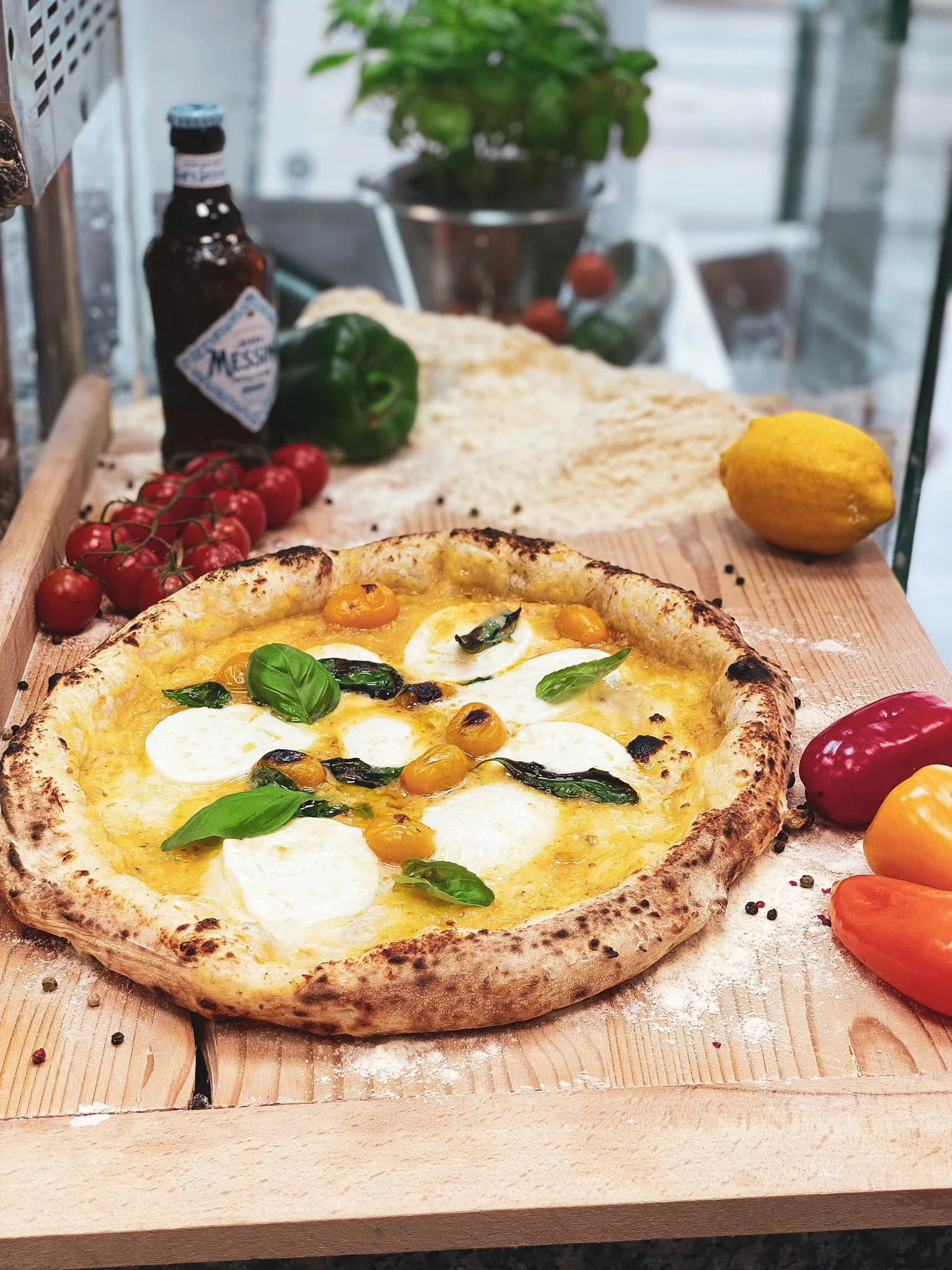 Appetitliche Pizza mit Mozzarella, Tomaten, Basilikum, Bier und Zitrone auf einem Holzbrett