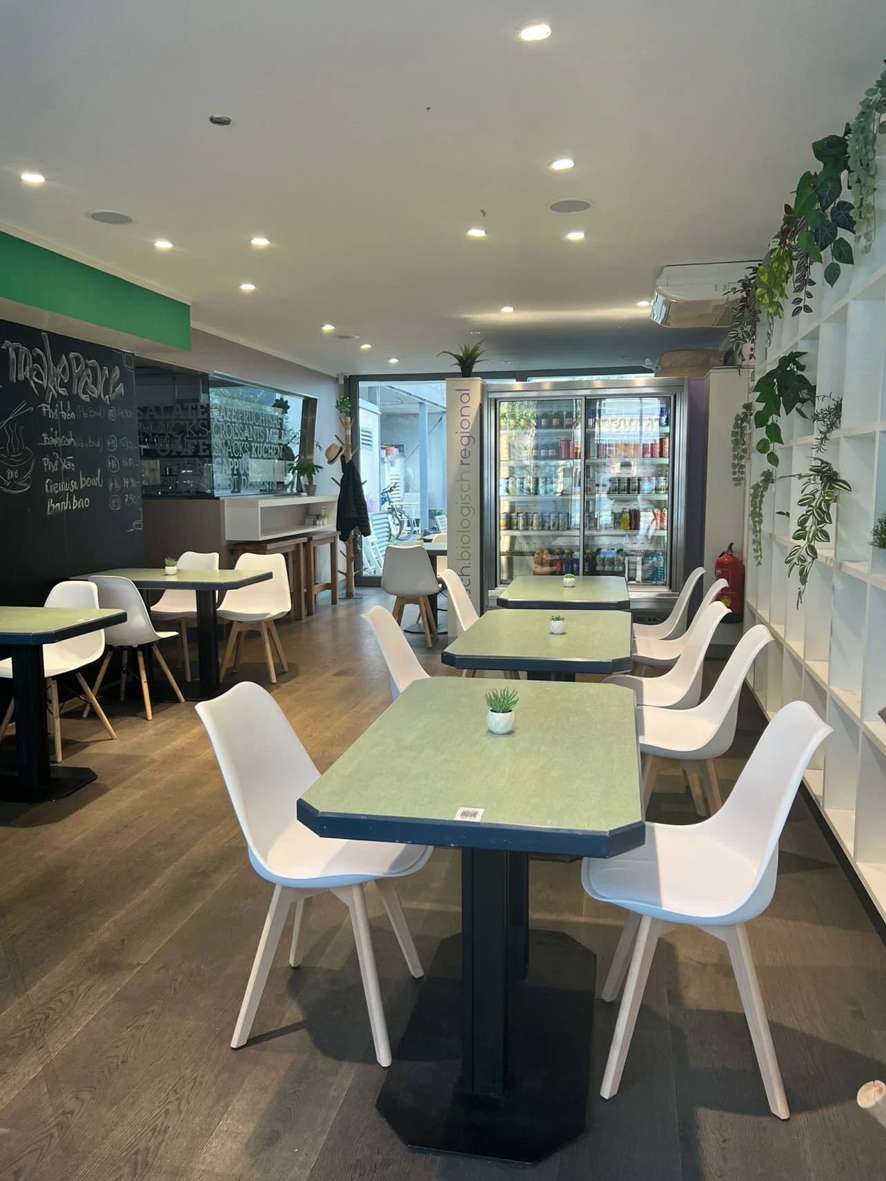 Restaurant-Interieur mit grünen Tischen, weißen Stühlen und Kreidetafel-Speisekarte.