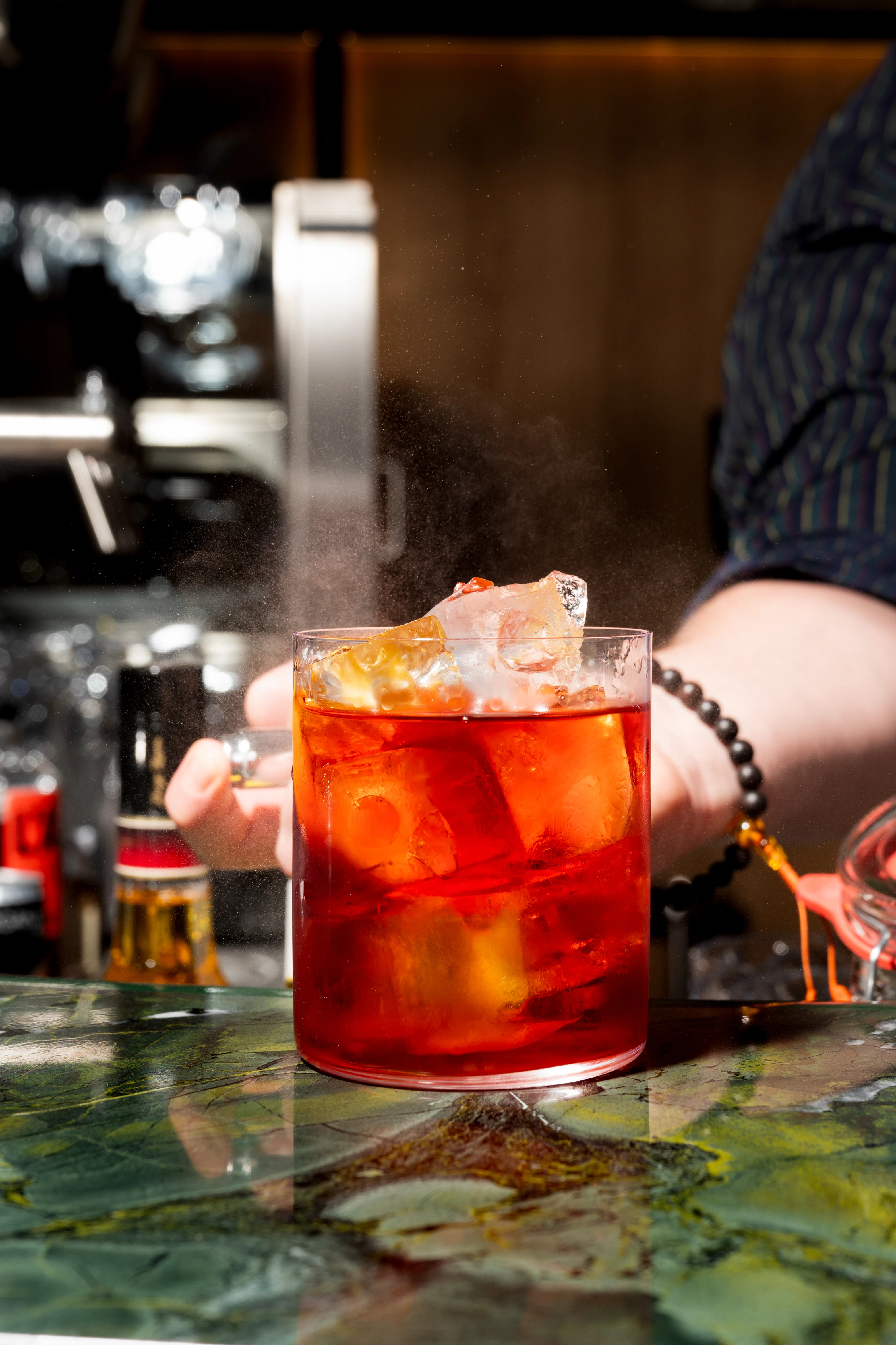 Negroni Cocktail auf einer Bar mit grünem Marmor, Barkeeper im Hintergrund.