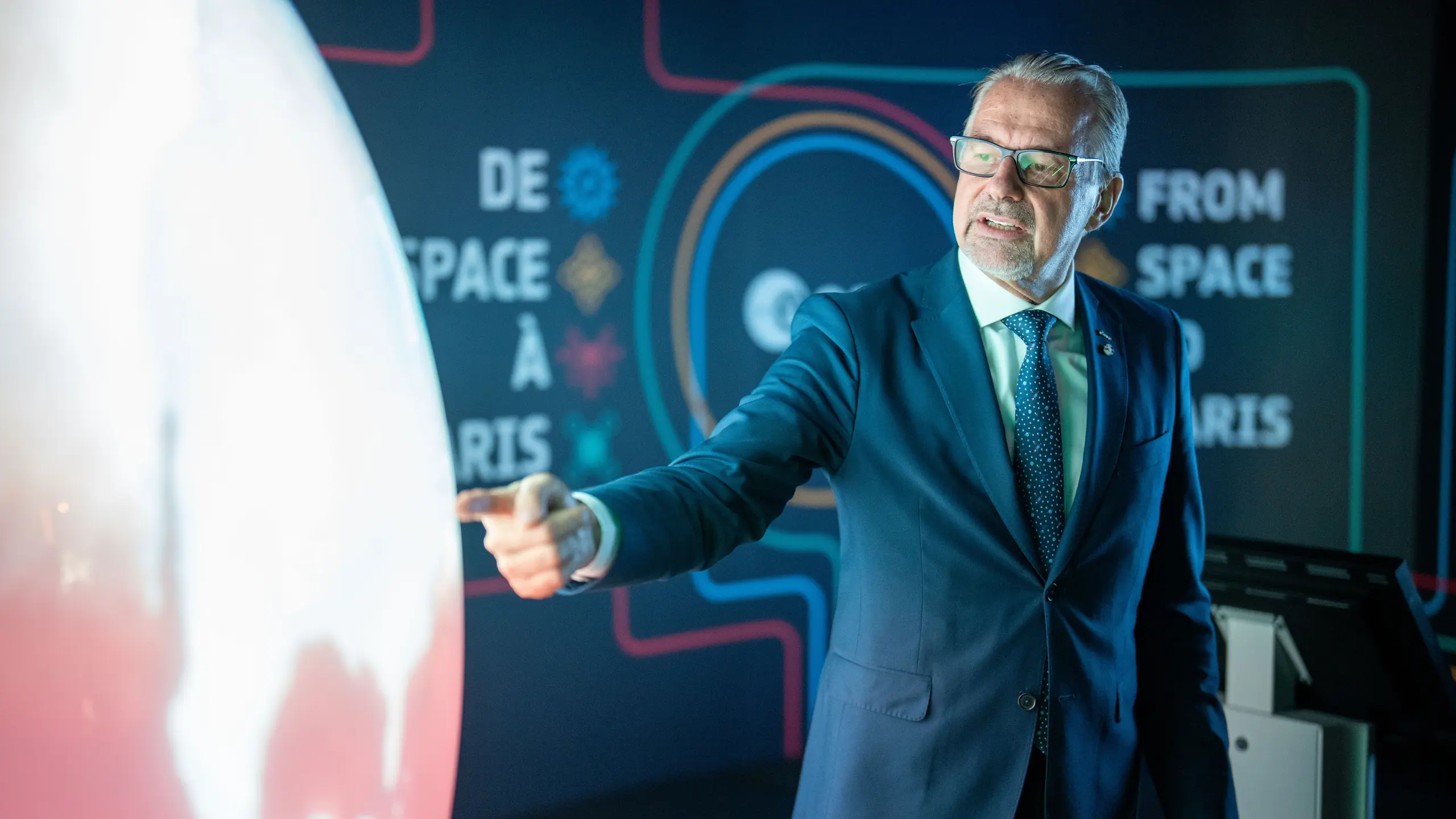 © APA/GEORG HOCHMUTH Mann, der auf einen großen Globus zeigt, vor schwarzem Hintergrund