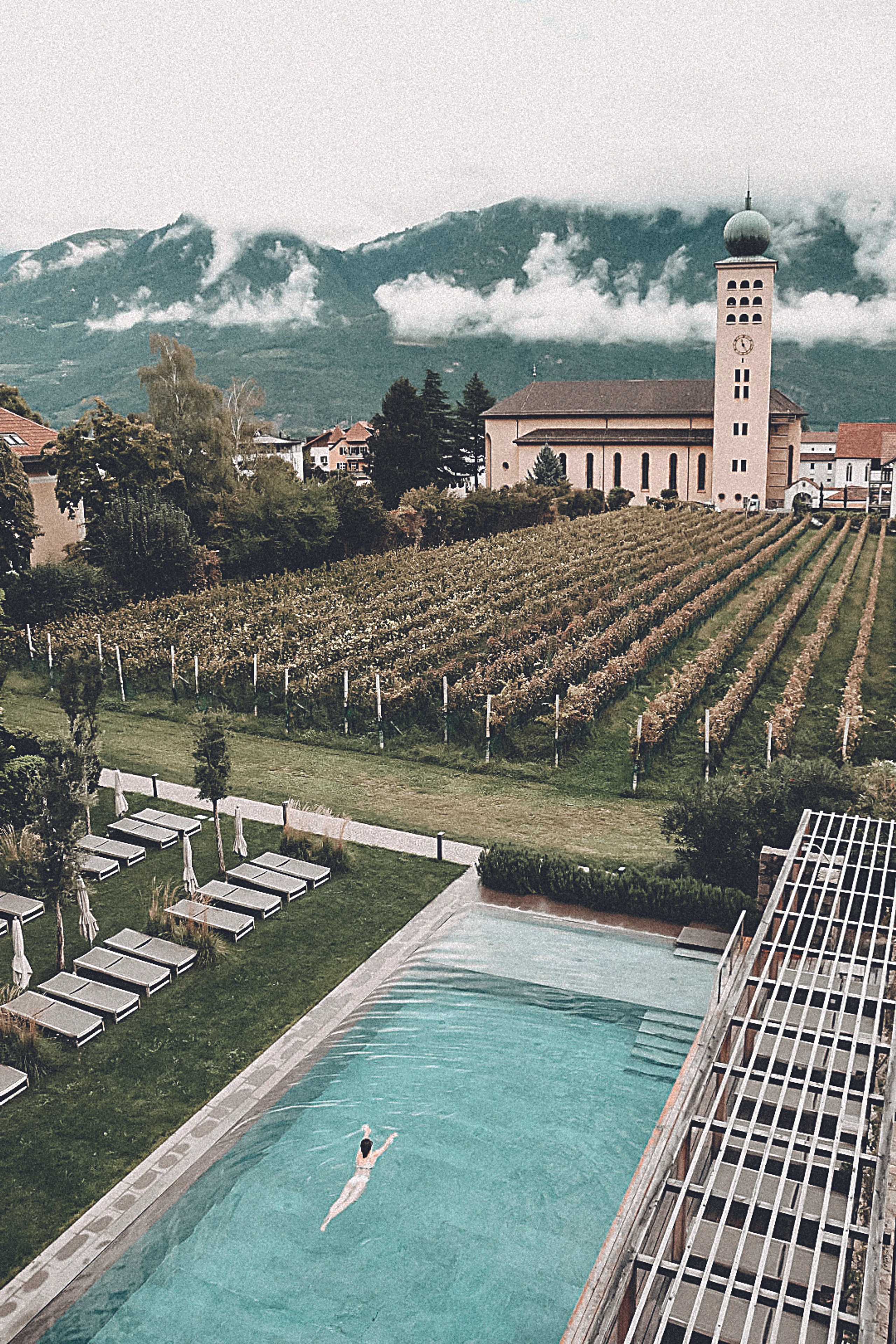 Swimmingpool umgeben von Äpfelbäumen, einer Kirchhe und Bergen