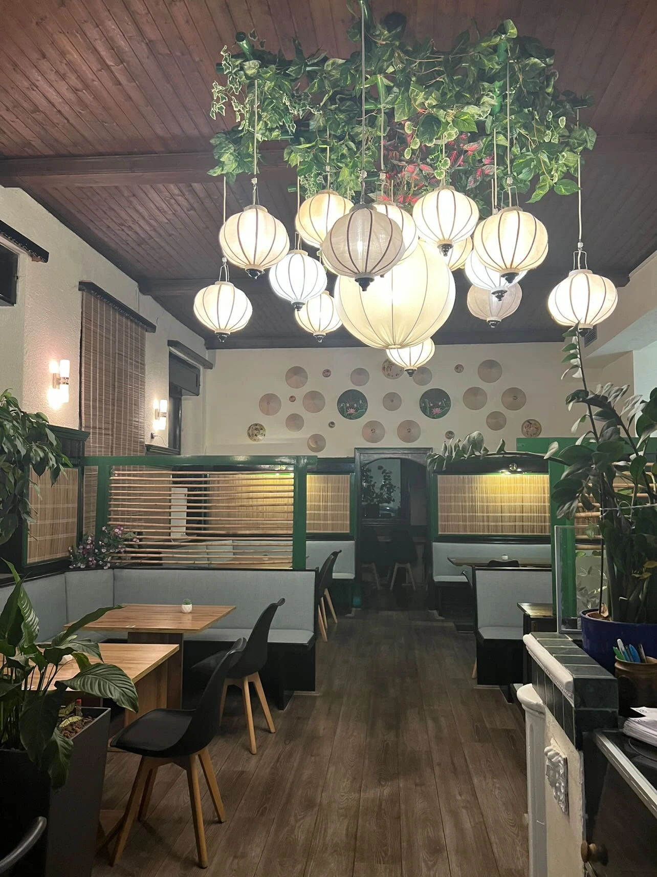 Gemütliches Restaurant-Interieur mit Tischen, Stühlen, Lampen, Pflanzen und Wanddekoration. Einladendes Ambiente mit asiatischem Touch.