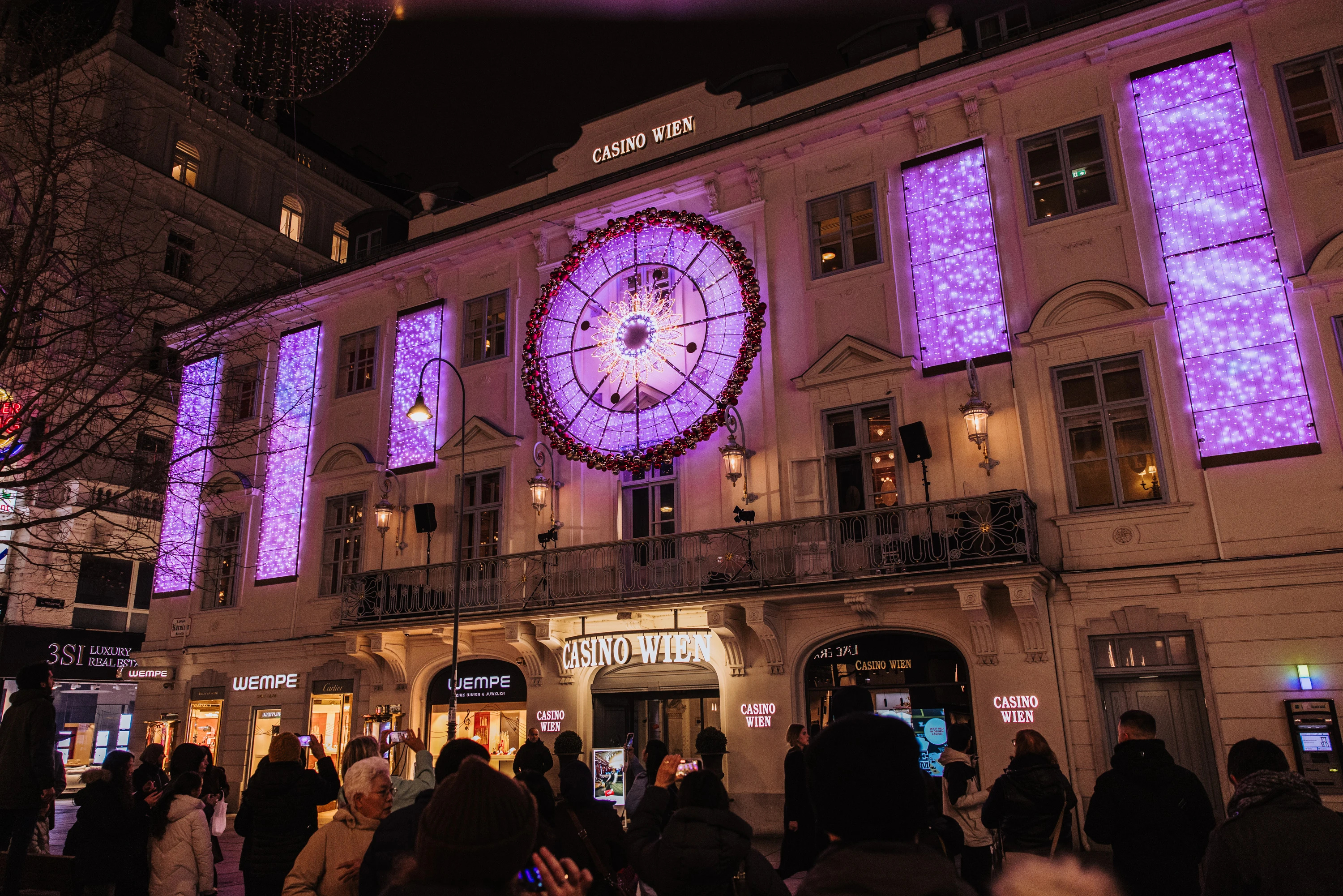Casino Wien at night, illuminated with purple Christmas lights and clock. Festive scene with people in Vienna, Austria.