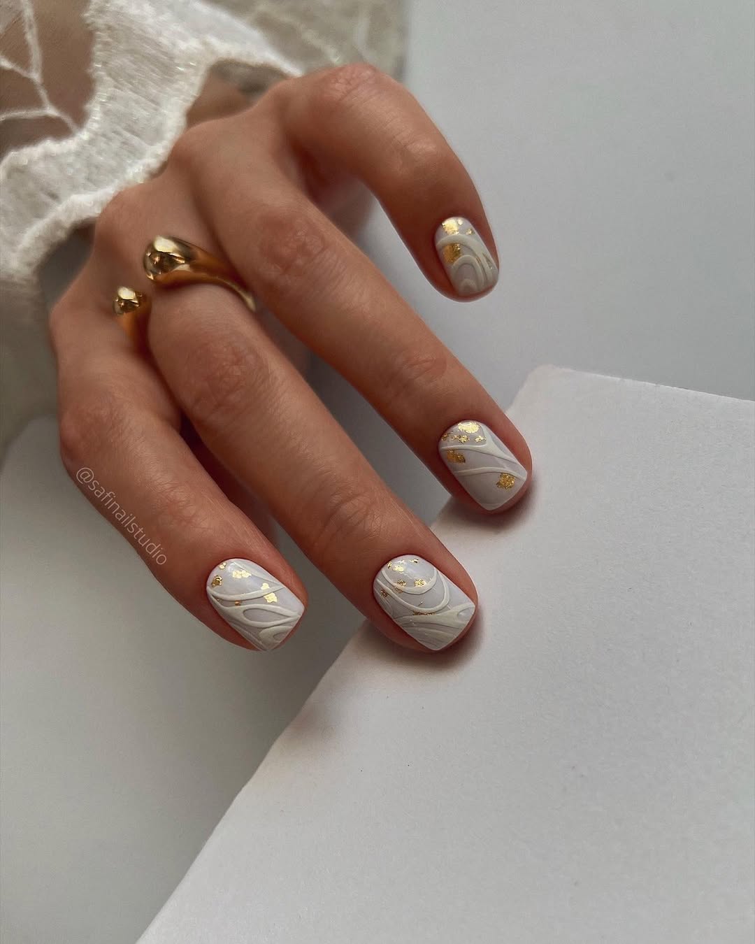 Bild von Maniküre: weiße Nägel mit weißen Liniendesigns und Gold-Plättchen-Details