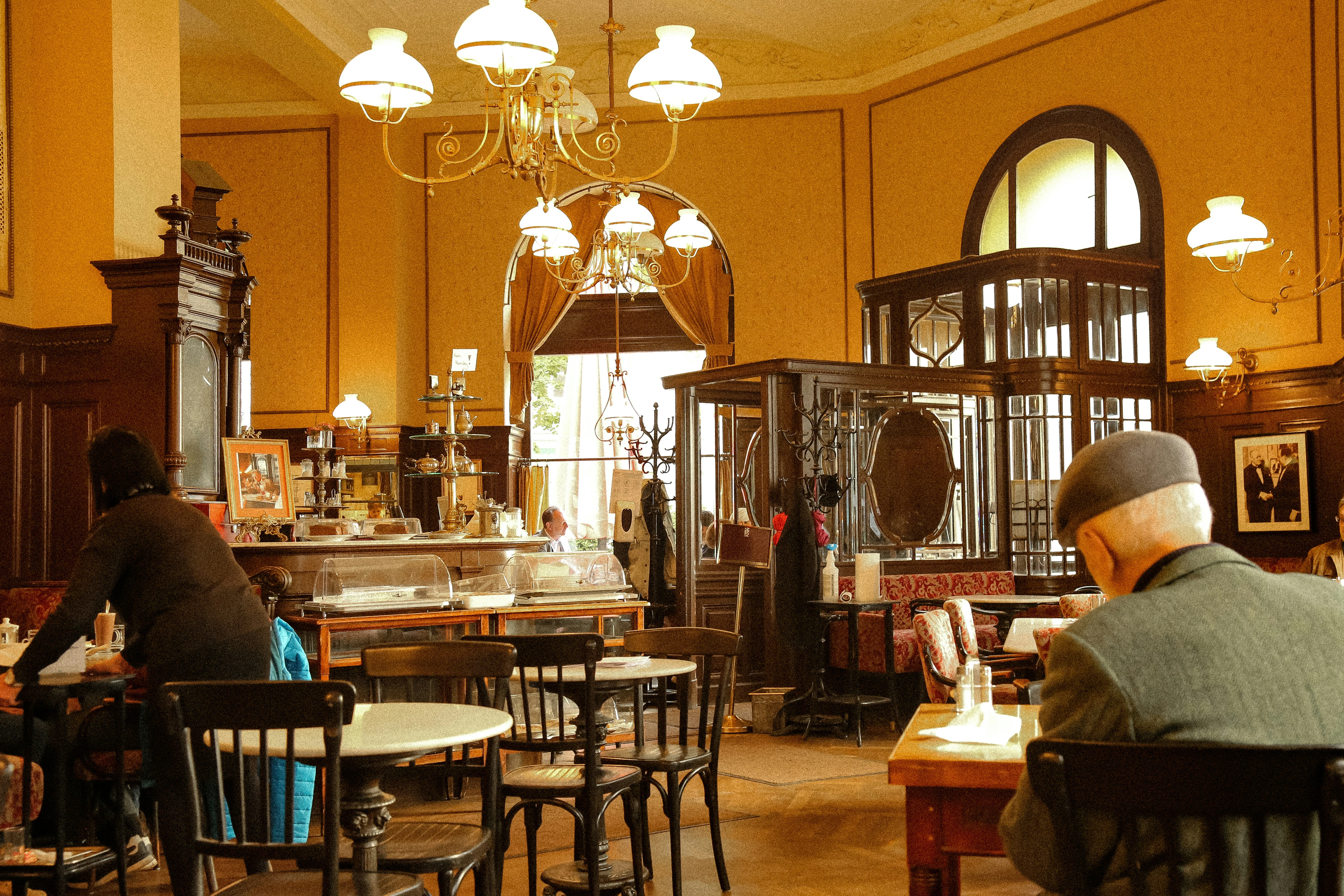 Interior view of a classic European cafe with patrons, pastries, and vintage decor.