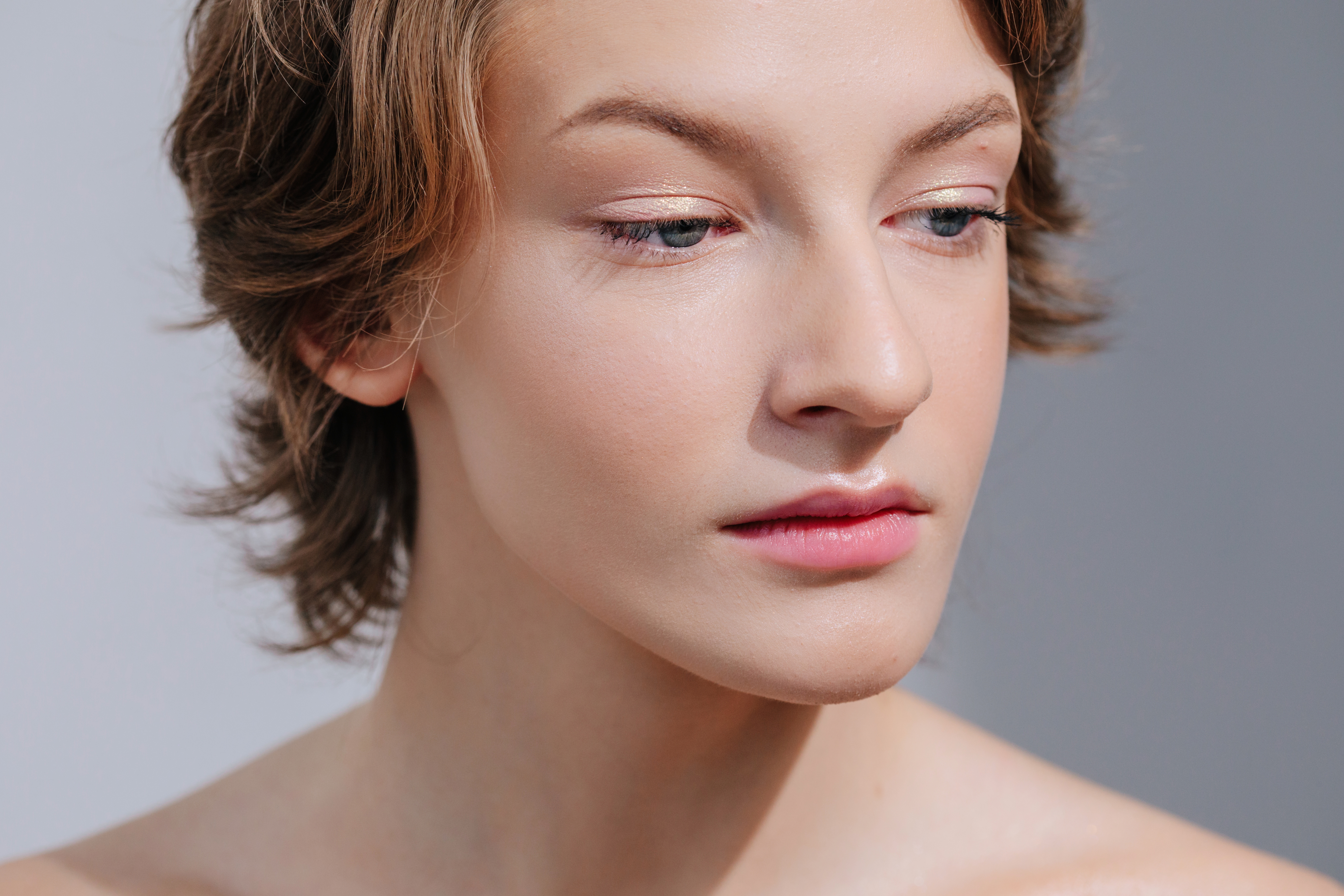 Close-Up von Model, das leicht zu Boden blickt mit grauem Hintergrund und minalem Make-up