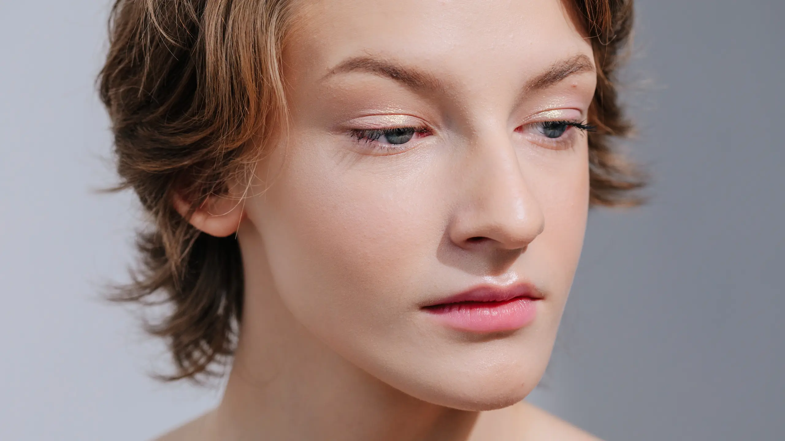 Close-Up von Model, das leicht zu Boden blickt mit grauem Hintergrund und minalem Make-up