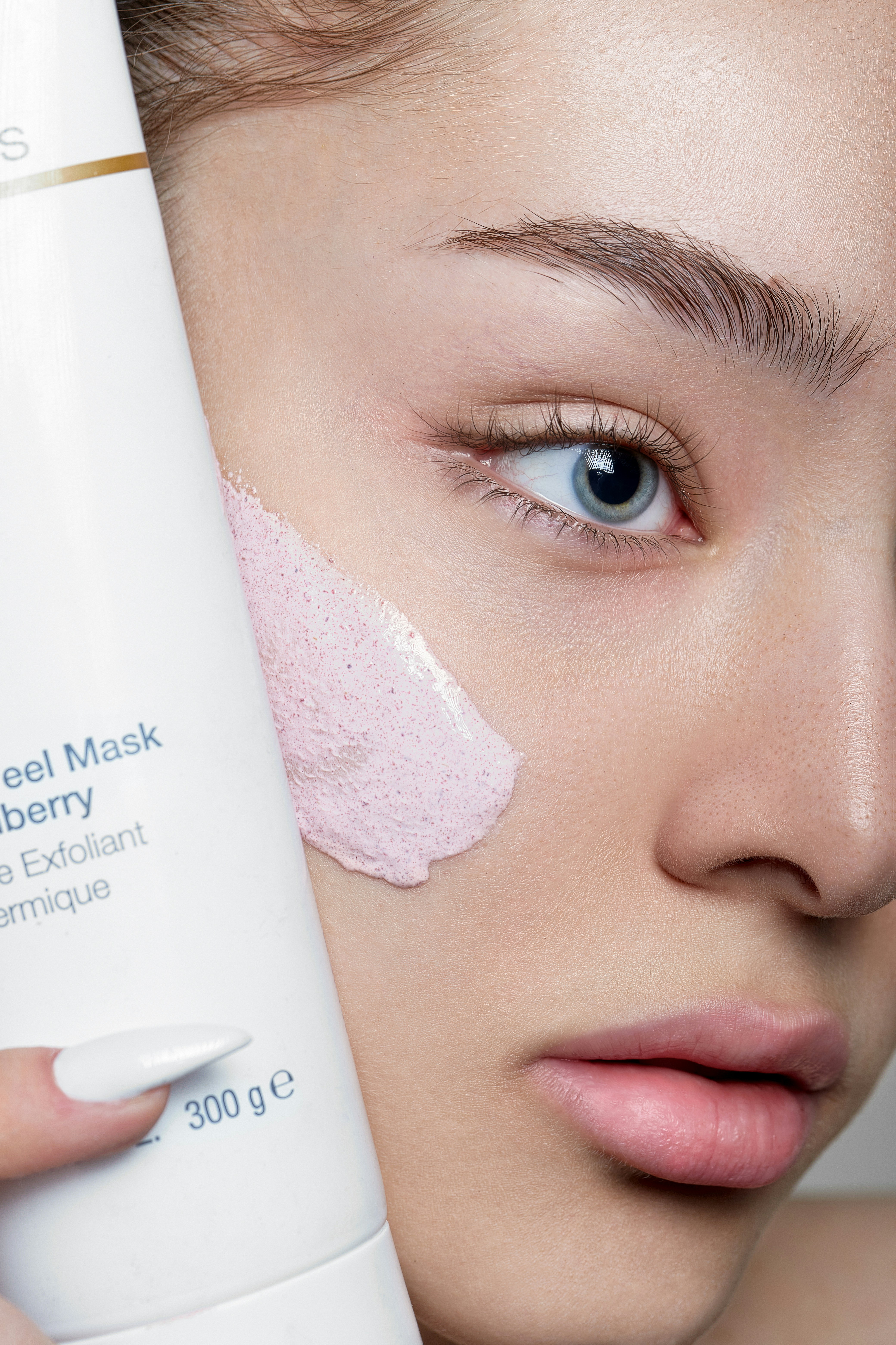 Close-Up von Frau mit Peeling-Maske im Gesicht und Produkt