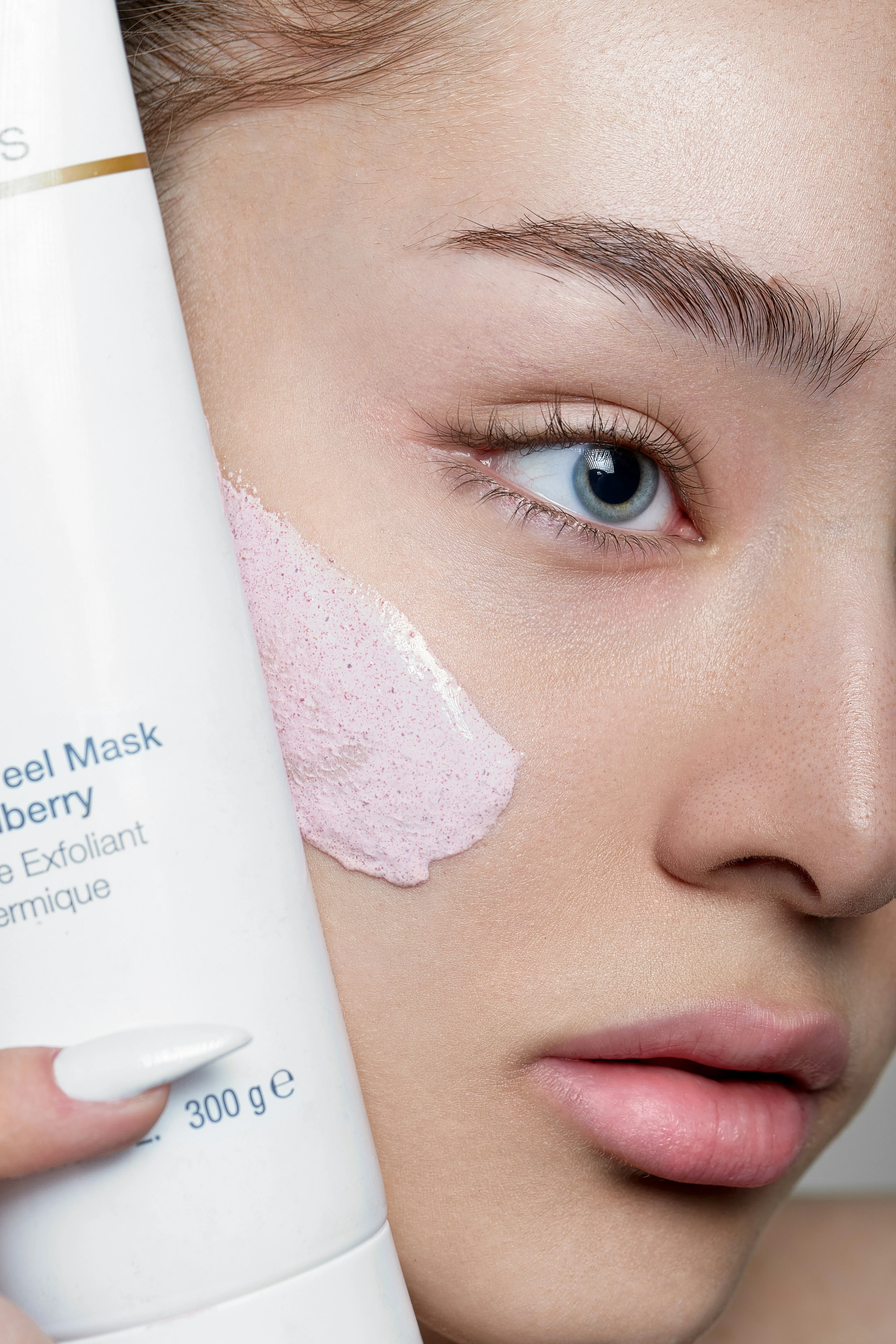 Close-Up von Frau mit Peeling-Maske im Gesicht und Produkt