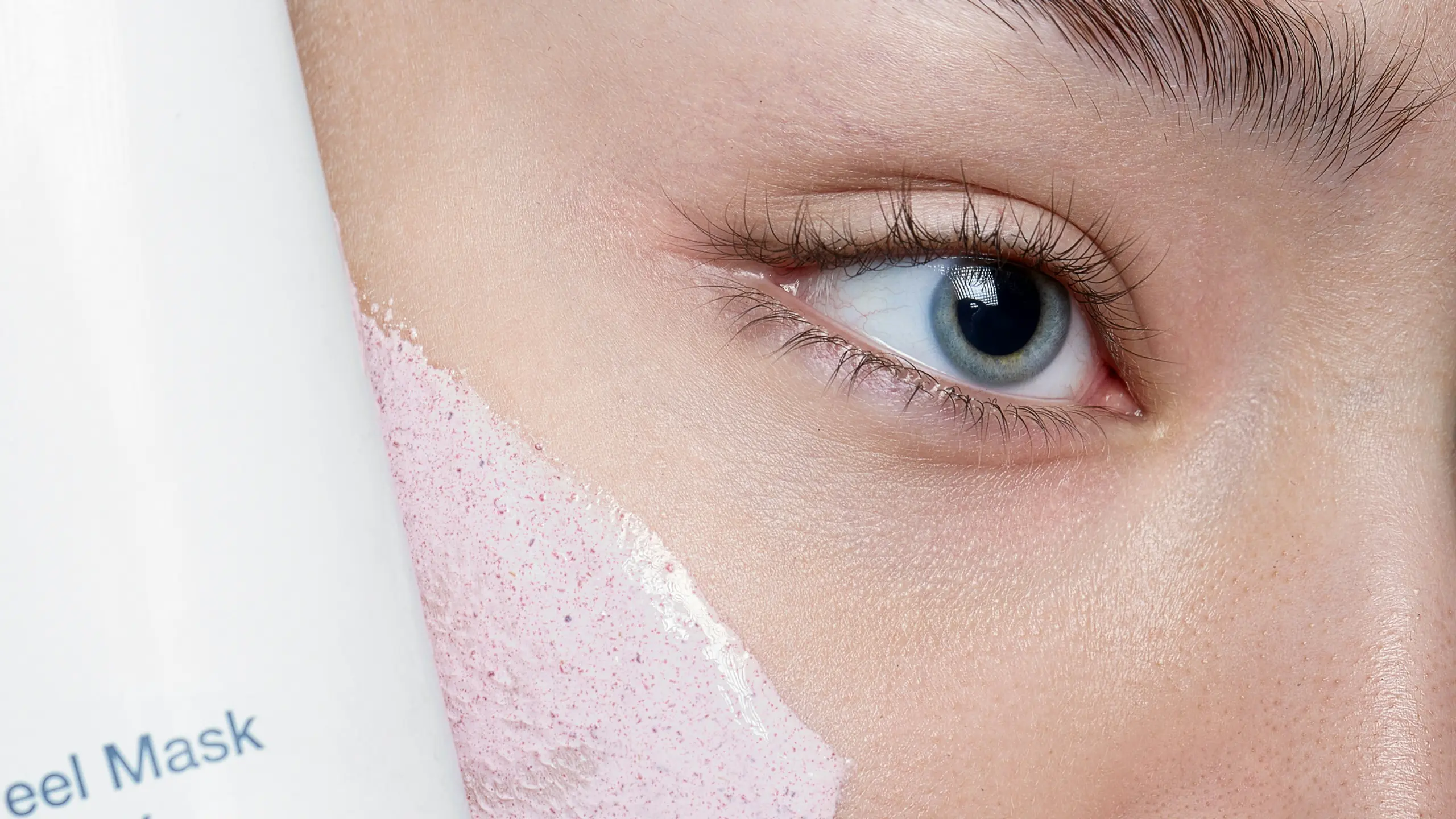 Close-Up von Frau mit Peeling-Maske im Gesicht und Produkt