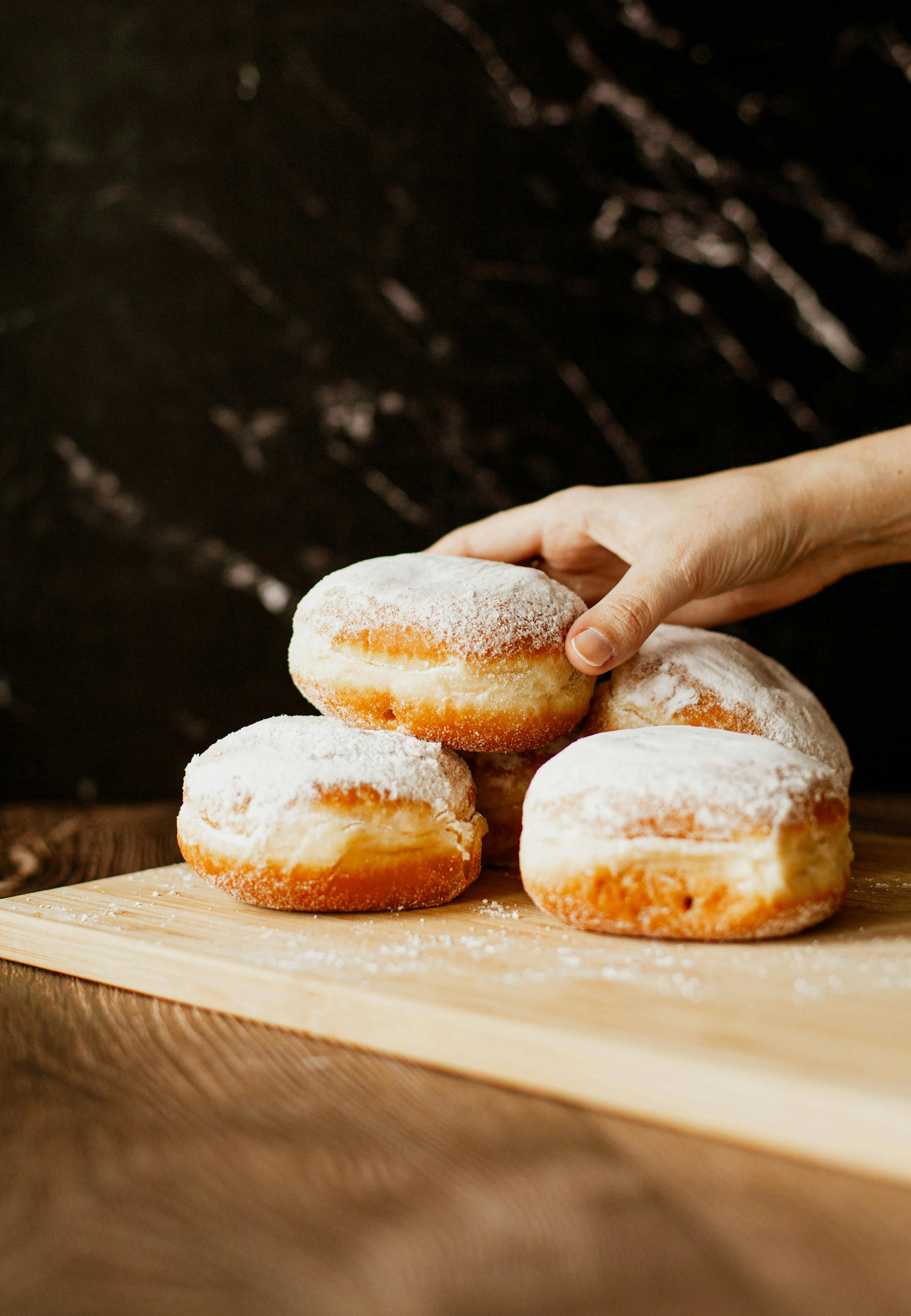 Stapel von Puderzucker-Krapfen auf einem Holzbrett, eine Hand greift nach einem.