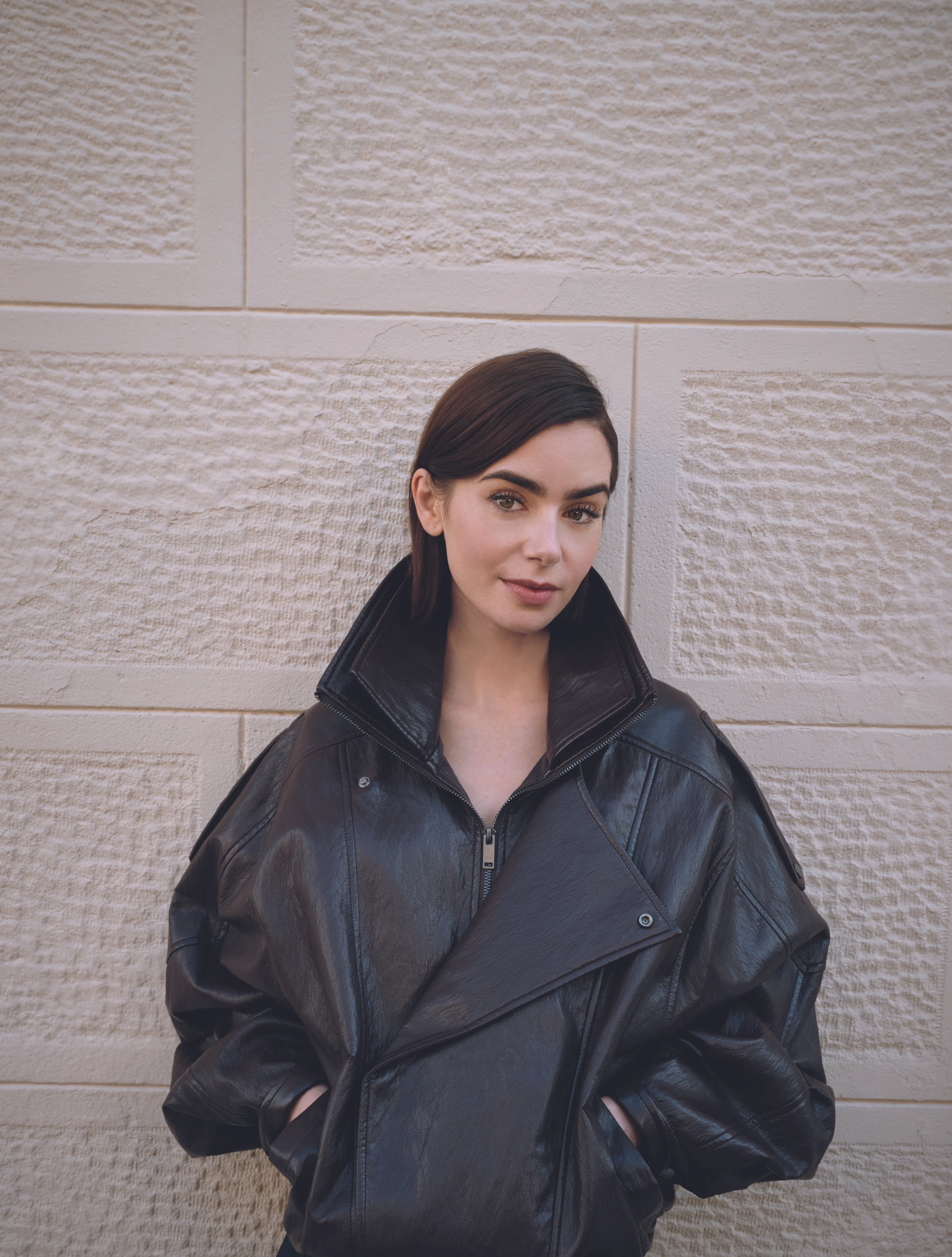 Lily Collins in schwarzer Lederjacke vor einer Mauer