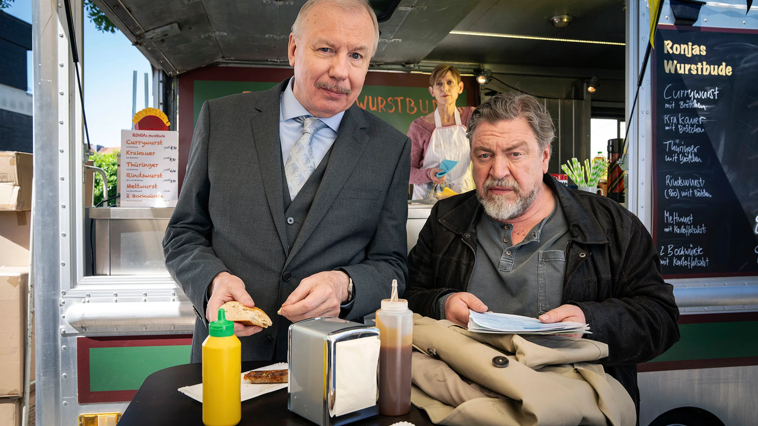 Armin Rohde und Ludger Pistor stehen vor einem Foodtruck und schauen in die Kamera