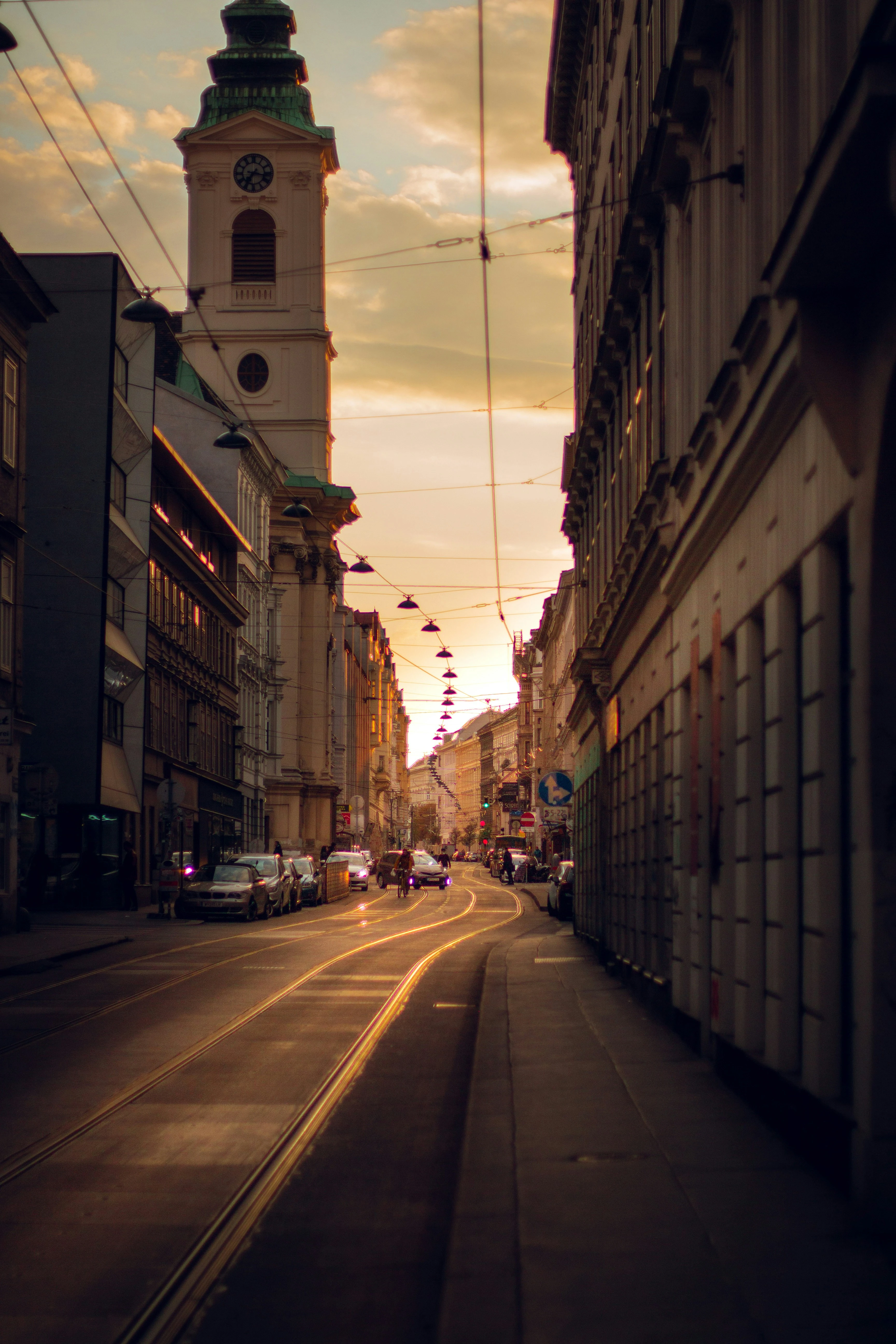 Blick auf eine Wiener Straße mit Straßenbahnlinien und einem Turm im Abendlicht.