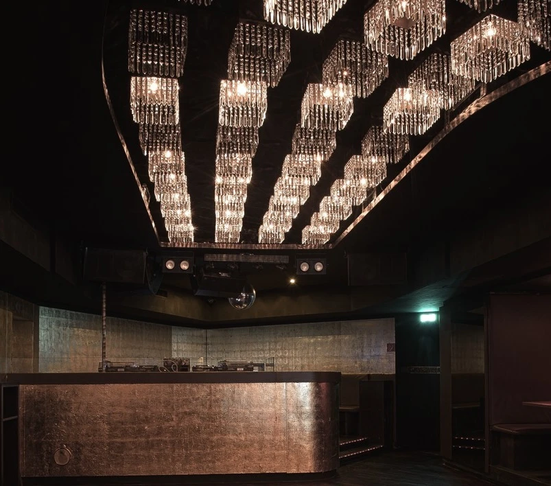 Innenaufnahme eines dunklen Nachtclubs mit Kronleuchtern und DJ-Pult