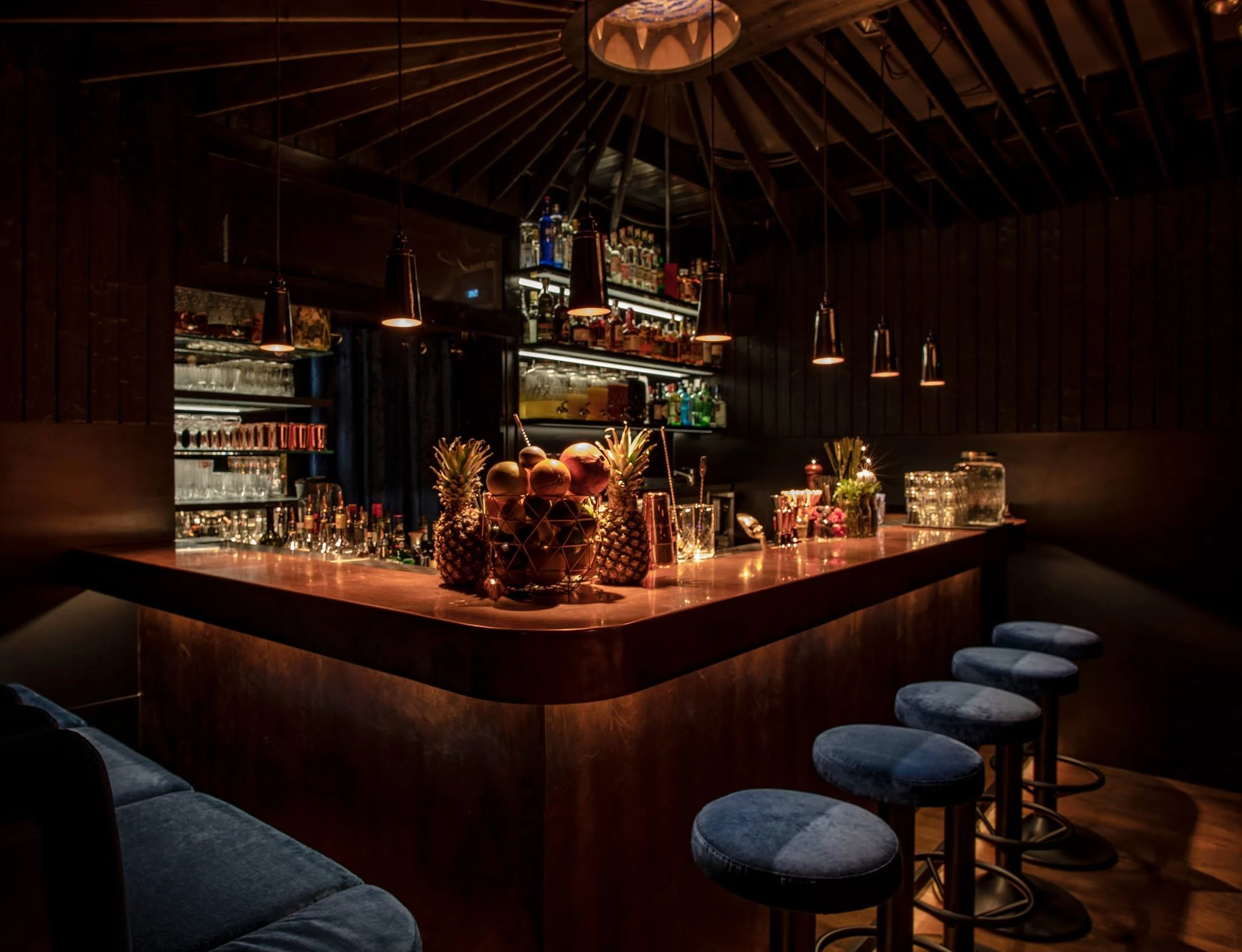 Bar mit Cocktails, Ananas und Barhockern in stimmungsvoller Beleuchtung.