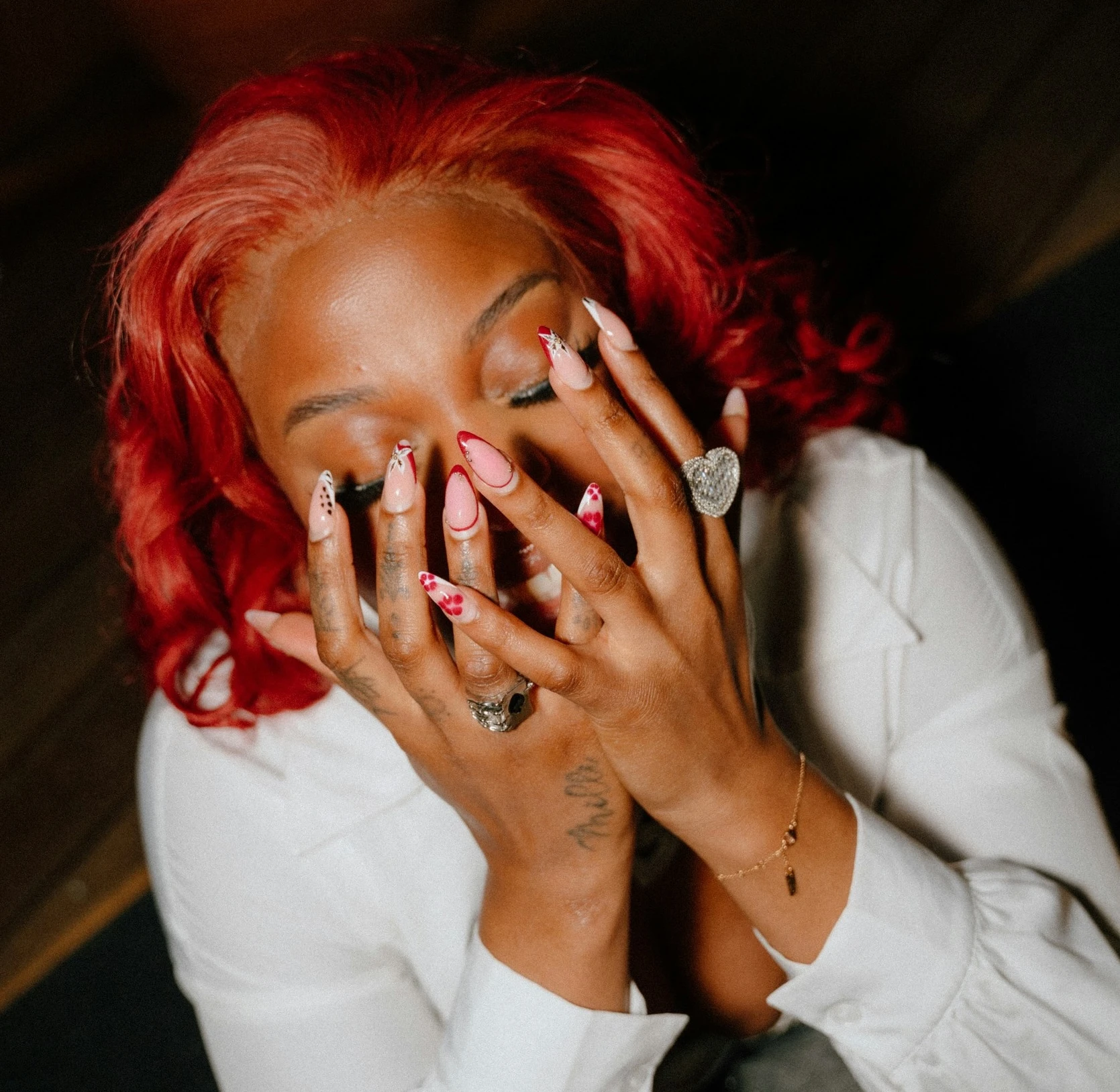 Frau mit rotem Haar bedeckt Gesicht mit Händen und auffälligem Nagellack