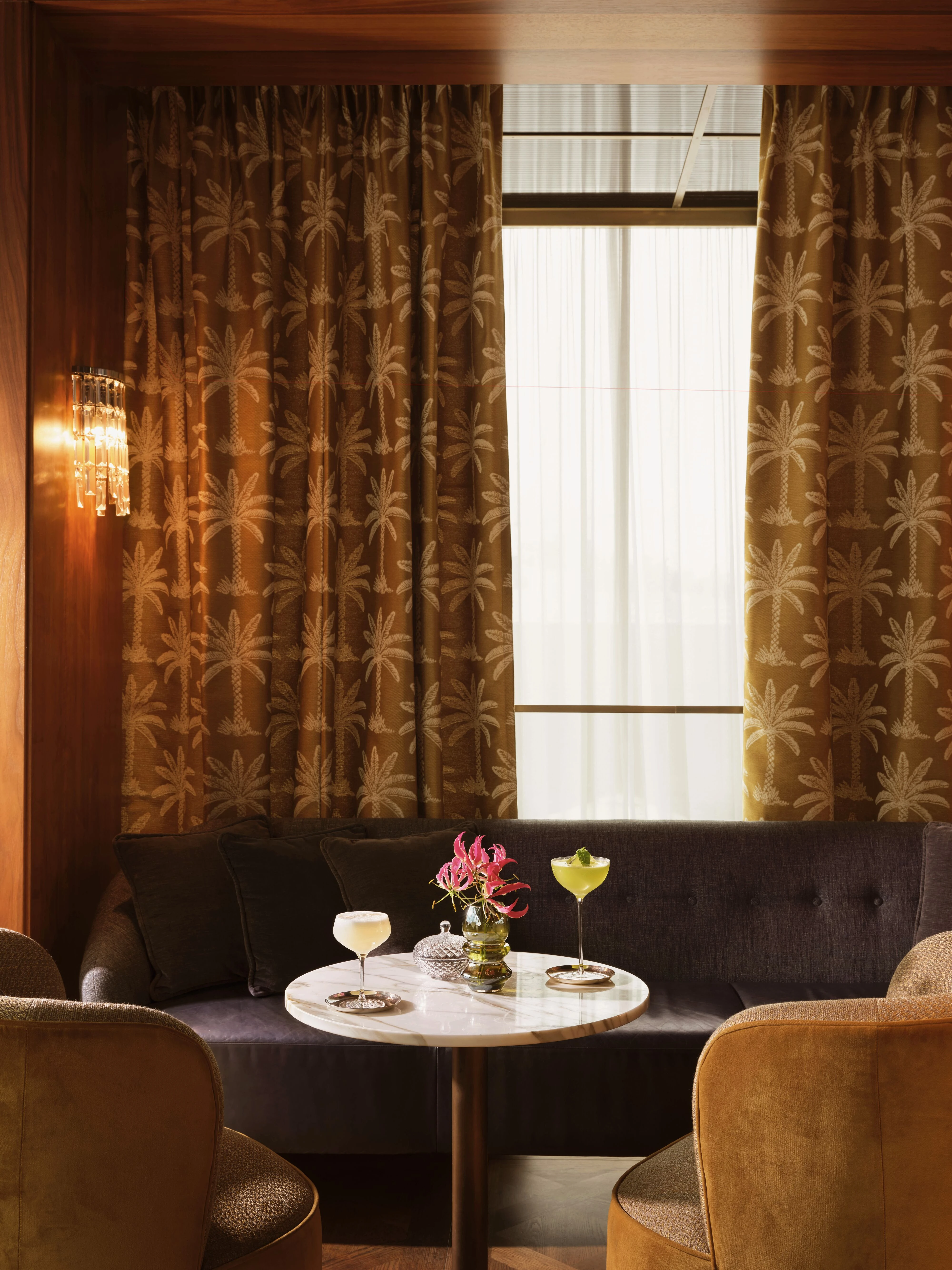 Cocktails auf einem Tisch in einer stilvollen Bar mit Palmendruck-Vorhängen.