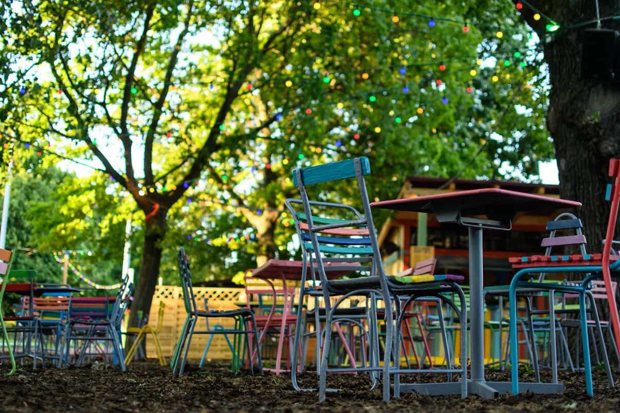 Farbenfrohe Gartenmöbel unter Bäumen mit Lichterketten