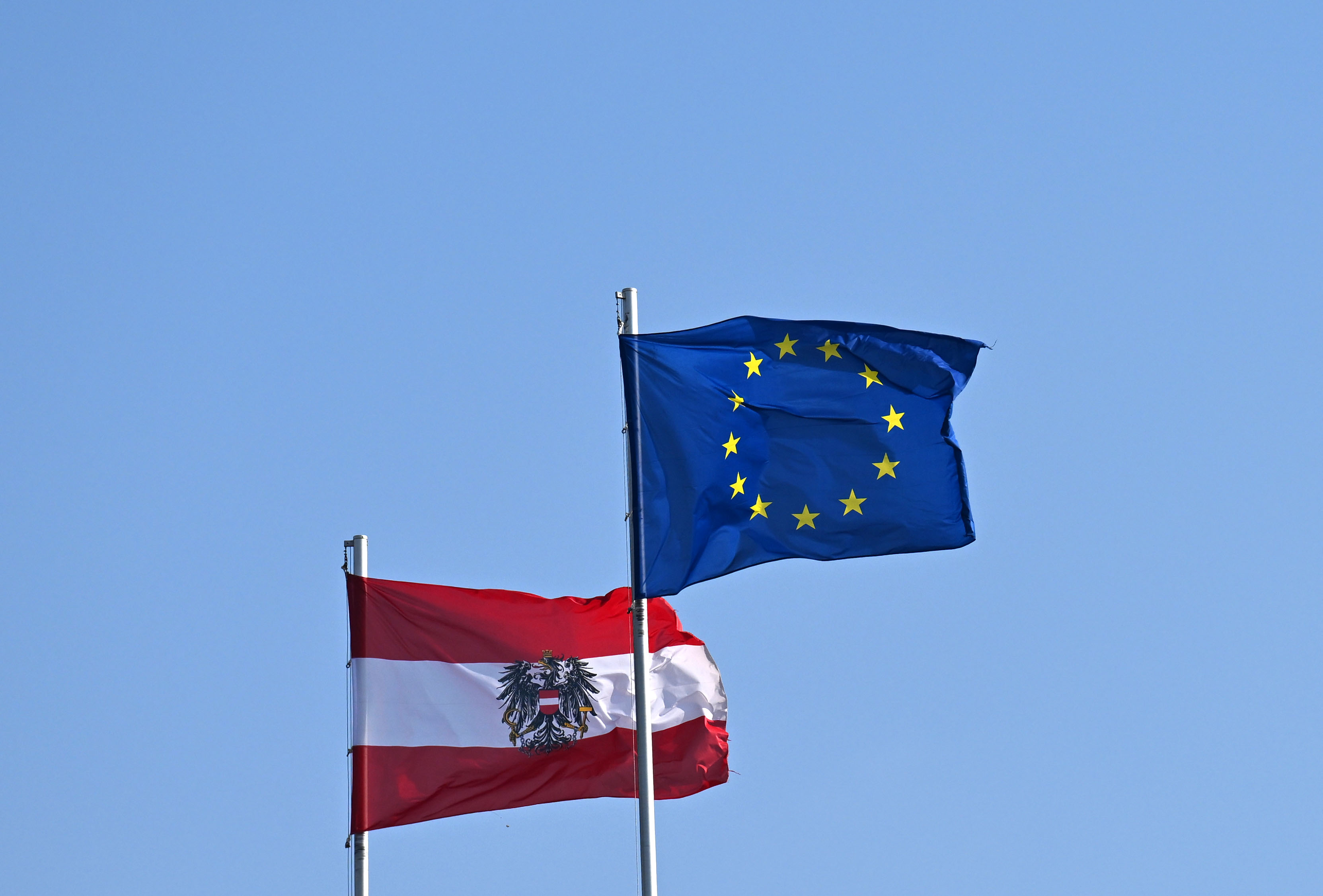 Österreich-Flagge und EU-Flagge vor blauem Himmel