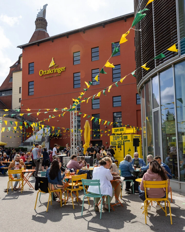 Ottakringer Brauerei Biergarten in Wien mit Menschen an Tischen und Flaggen