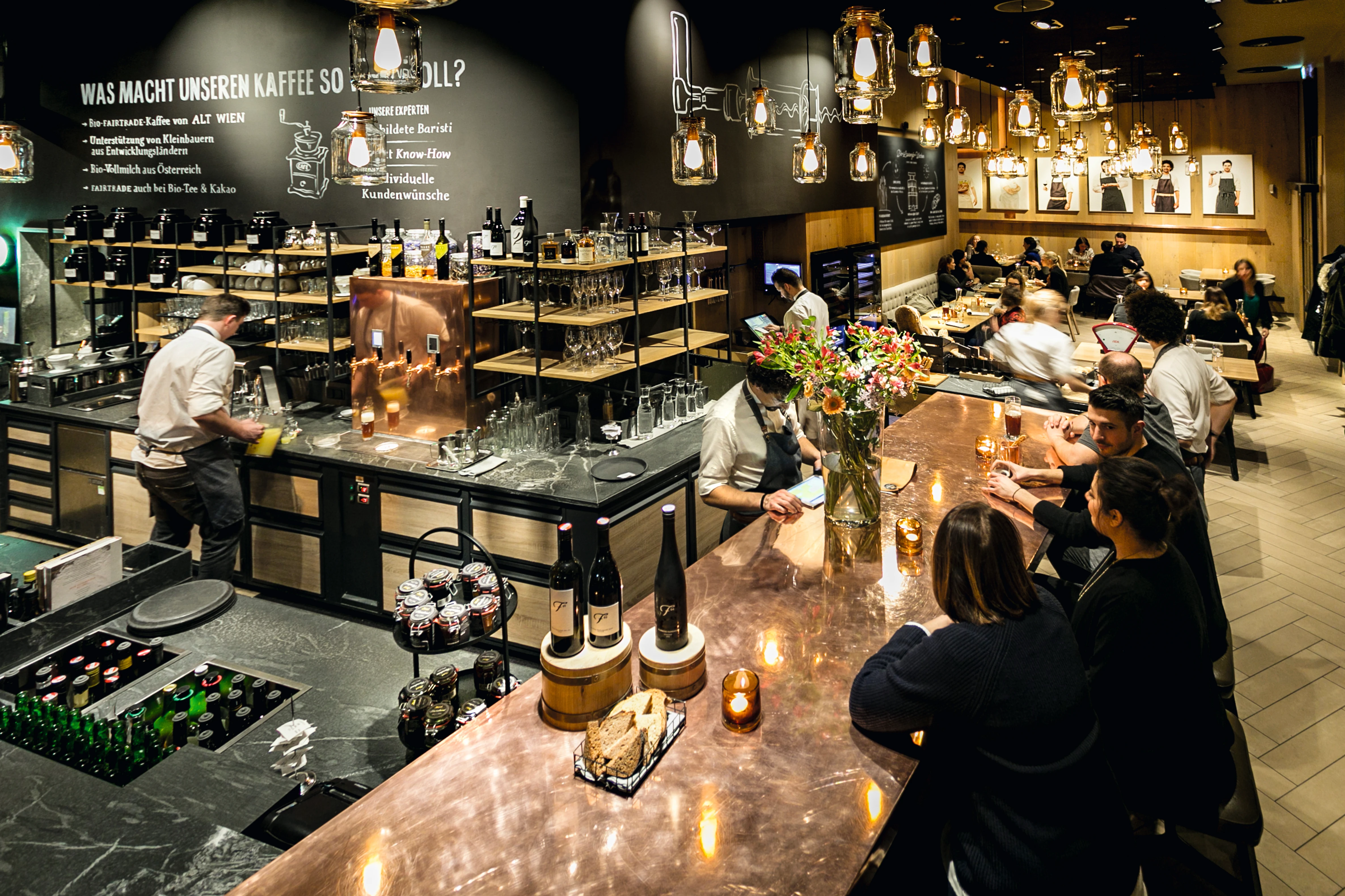 Lebhaftes Café-Interieur mit Gästen, Bar und Personal bei der Arbeit.