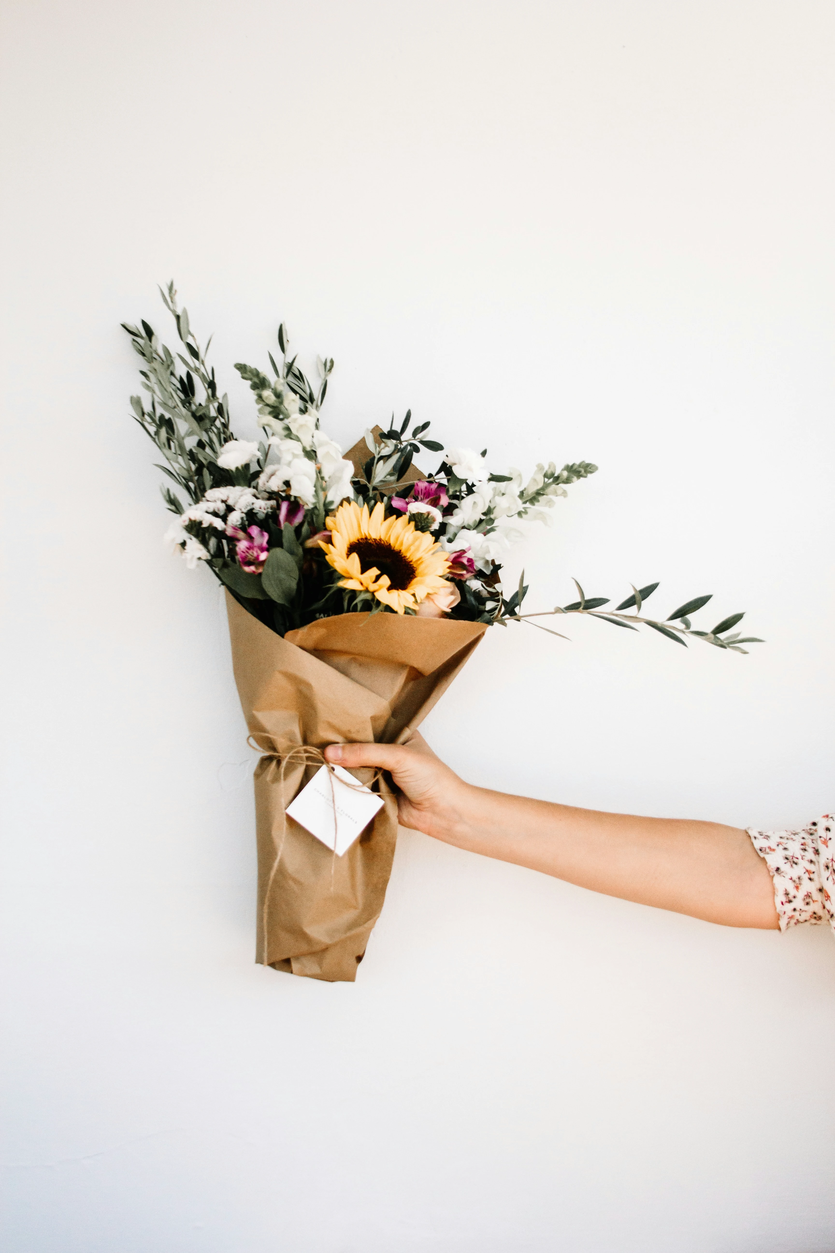 Hand hält Blumenstrauß mit Sonnenblume in Papier gewickelt