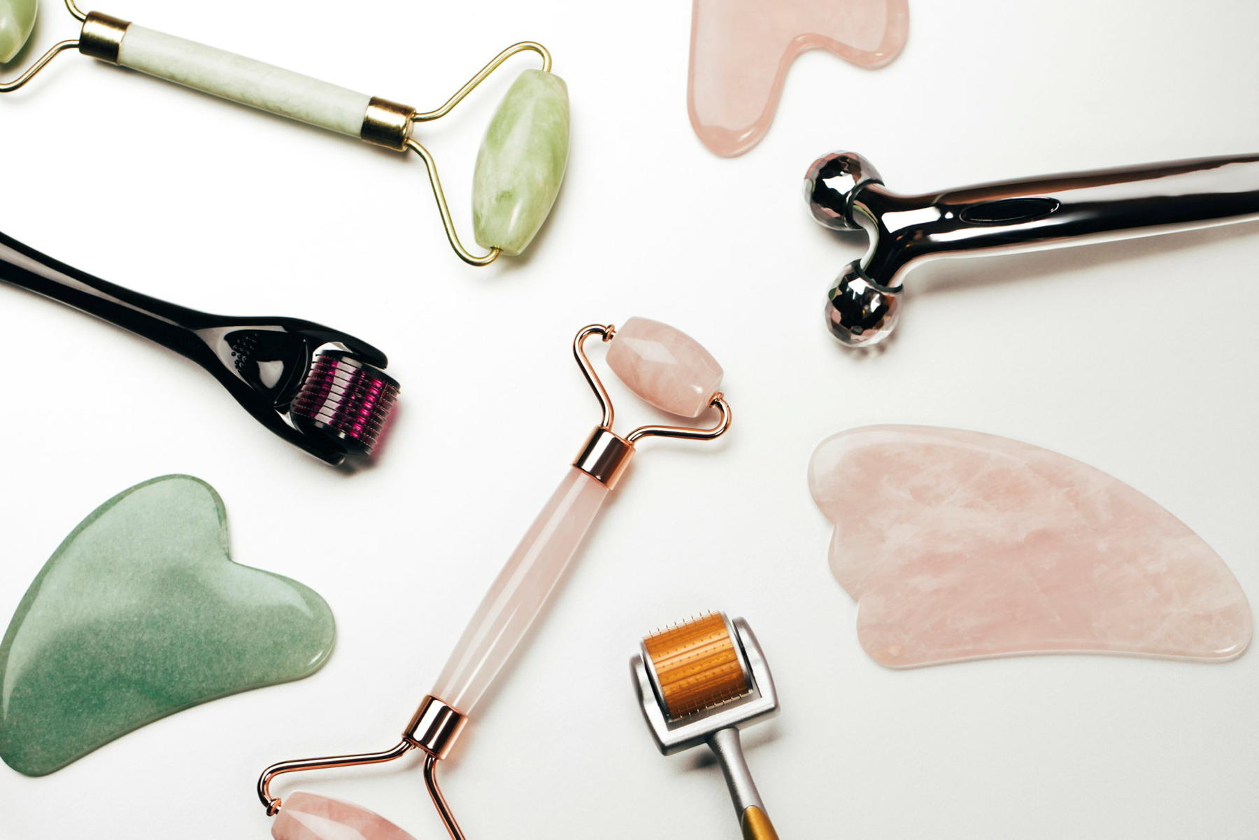 Mehrere Tools (Gua Sha, Jaderoller und Co.) liegen auf einer weißen Fläche