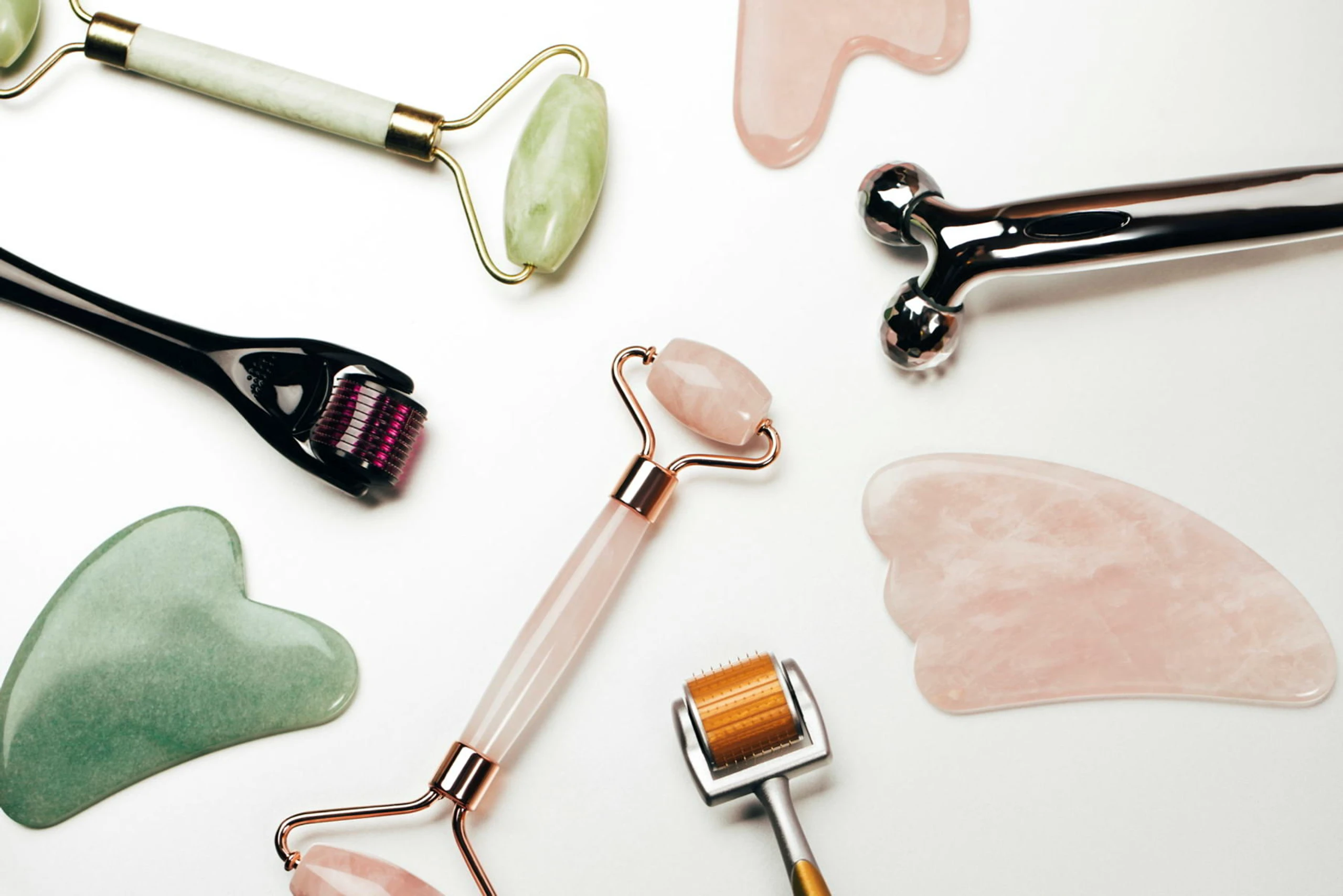 Mehrere Tools (Gua Sha, Jaderoller und Co.) liegen auf einer weißen Fläche