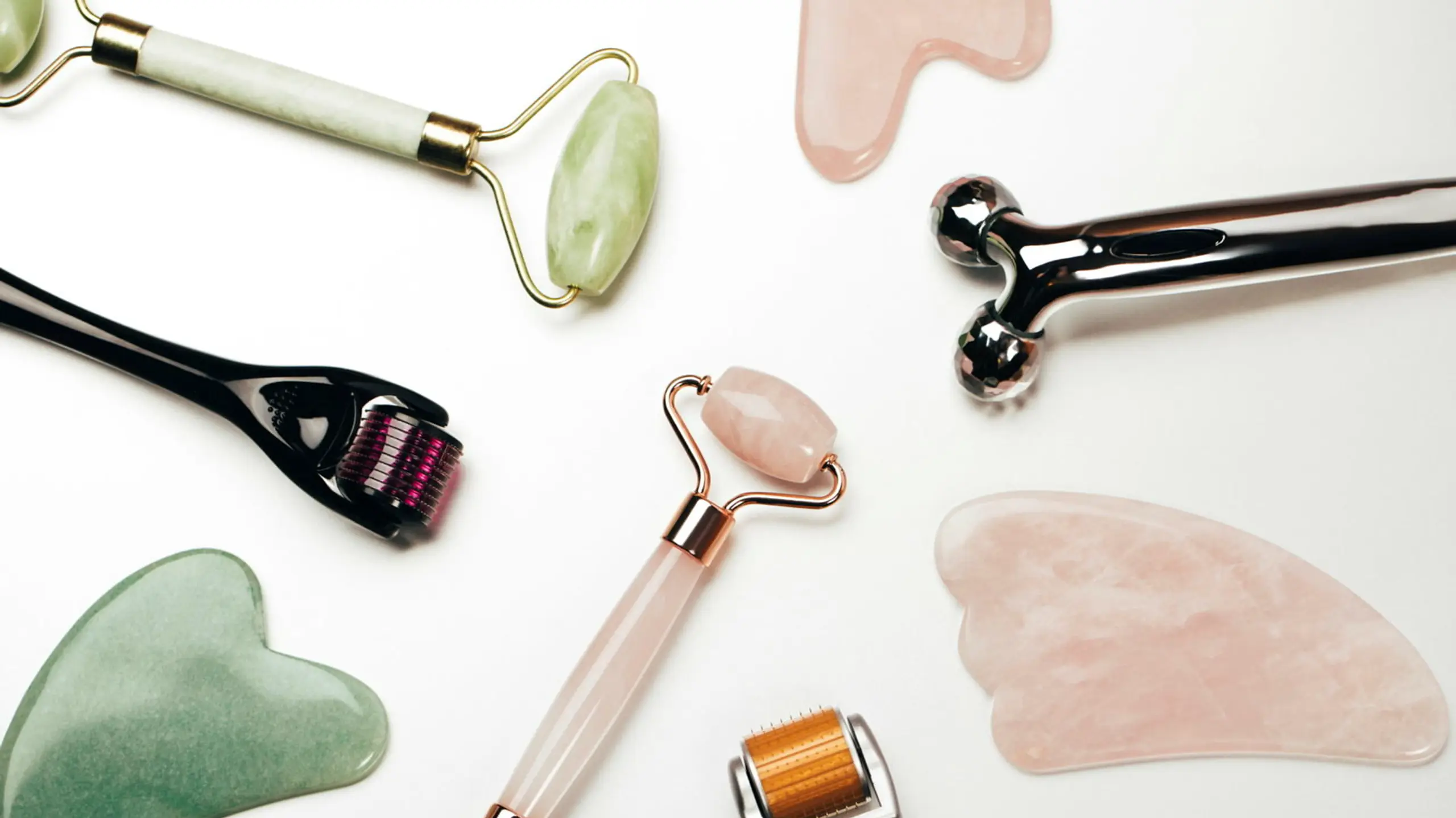 Mehrere Tools (Gua Sha, Jaderoller und Co.) liegen auf einer weißen Fläche
