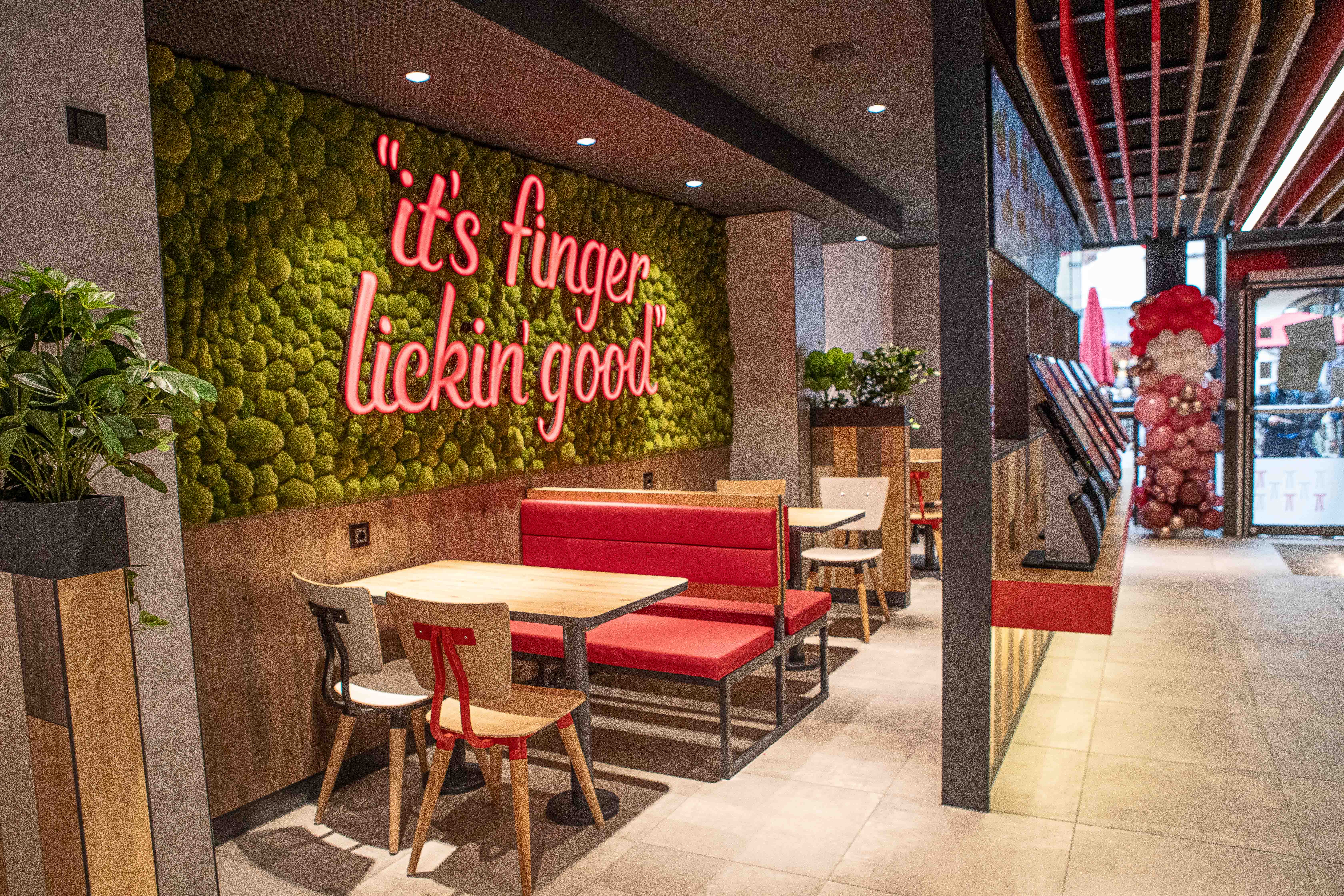 Sitzbereich der KFC-Filiale Villach mit Moosbild und Schriftzug „it's finger lickin' good“