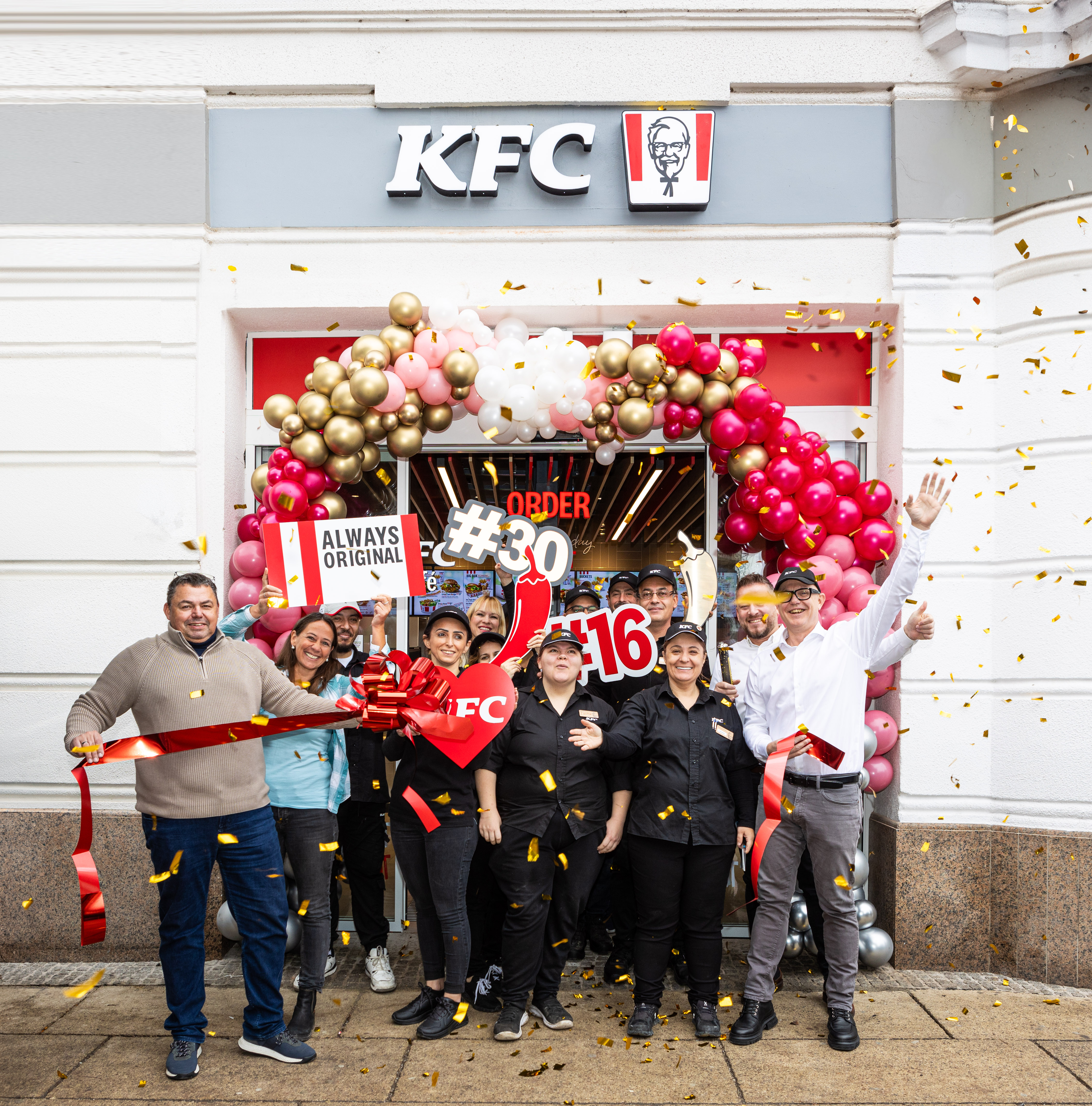 Team durchschneidet das rote Eröffnungsband einer KFC-Filiale unter Konfettiregen