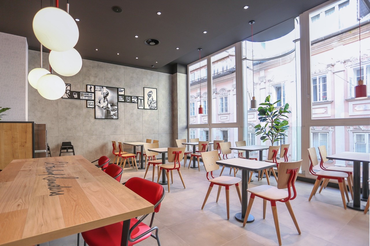 Sitzbereich eines KFC-Restaurants mit roten Stühlen, Holztischen und großen Fensterfronten