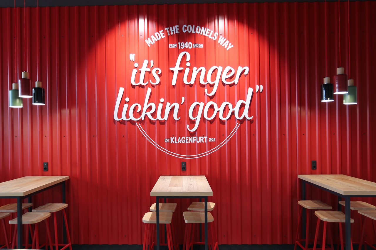 Wandschriftzug 'It's Finger Lickin' Good' im KFC-Restaurant Klagenfurt, dahinter Sitzbereich
