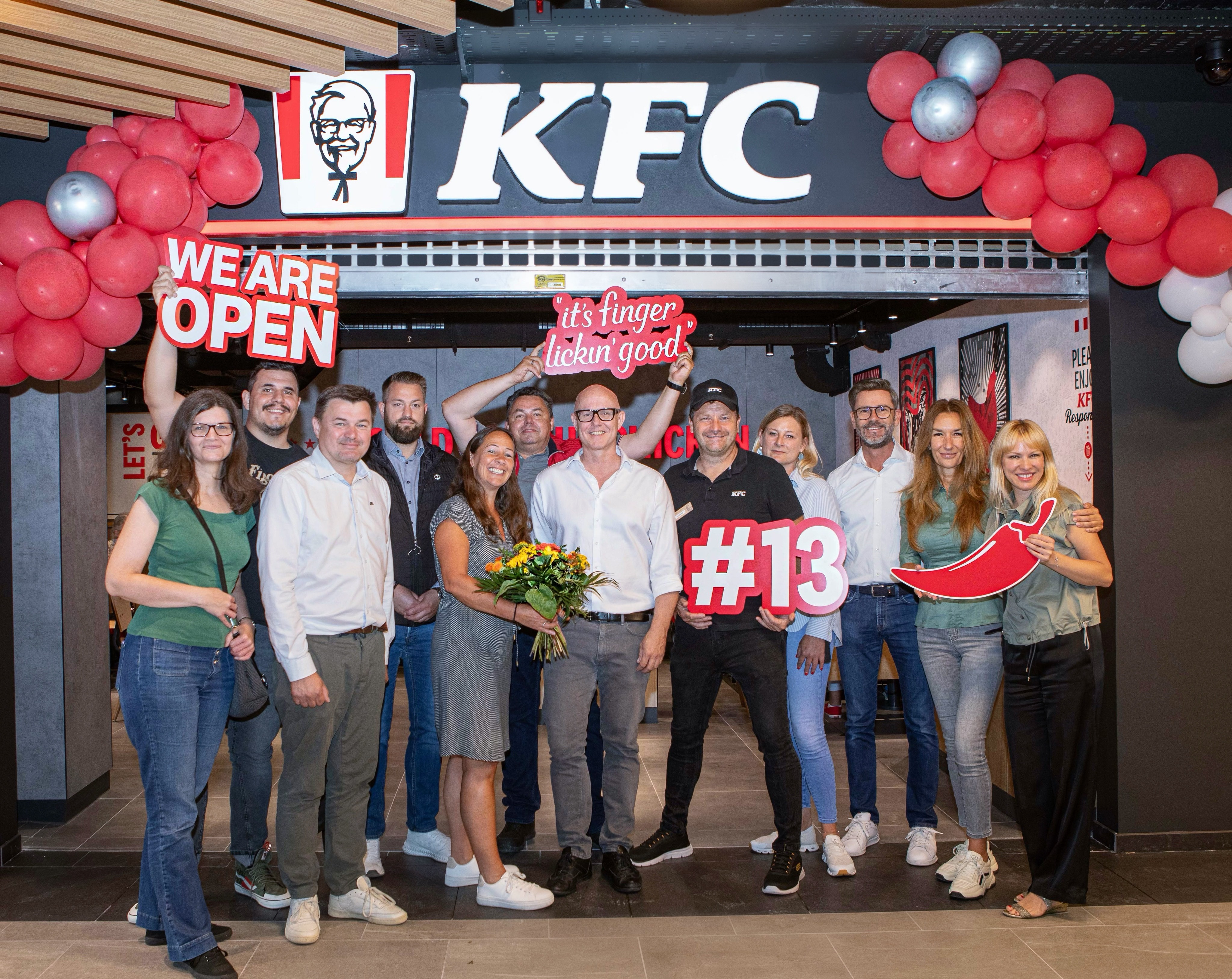 Eröffnung der KFC-Filiale Amstetten: Team posiert mit Blumenstrauß und Schild „#13“
