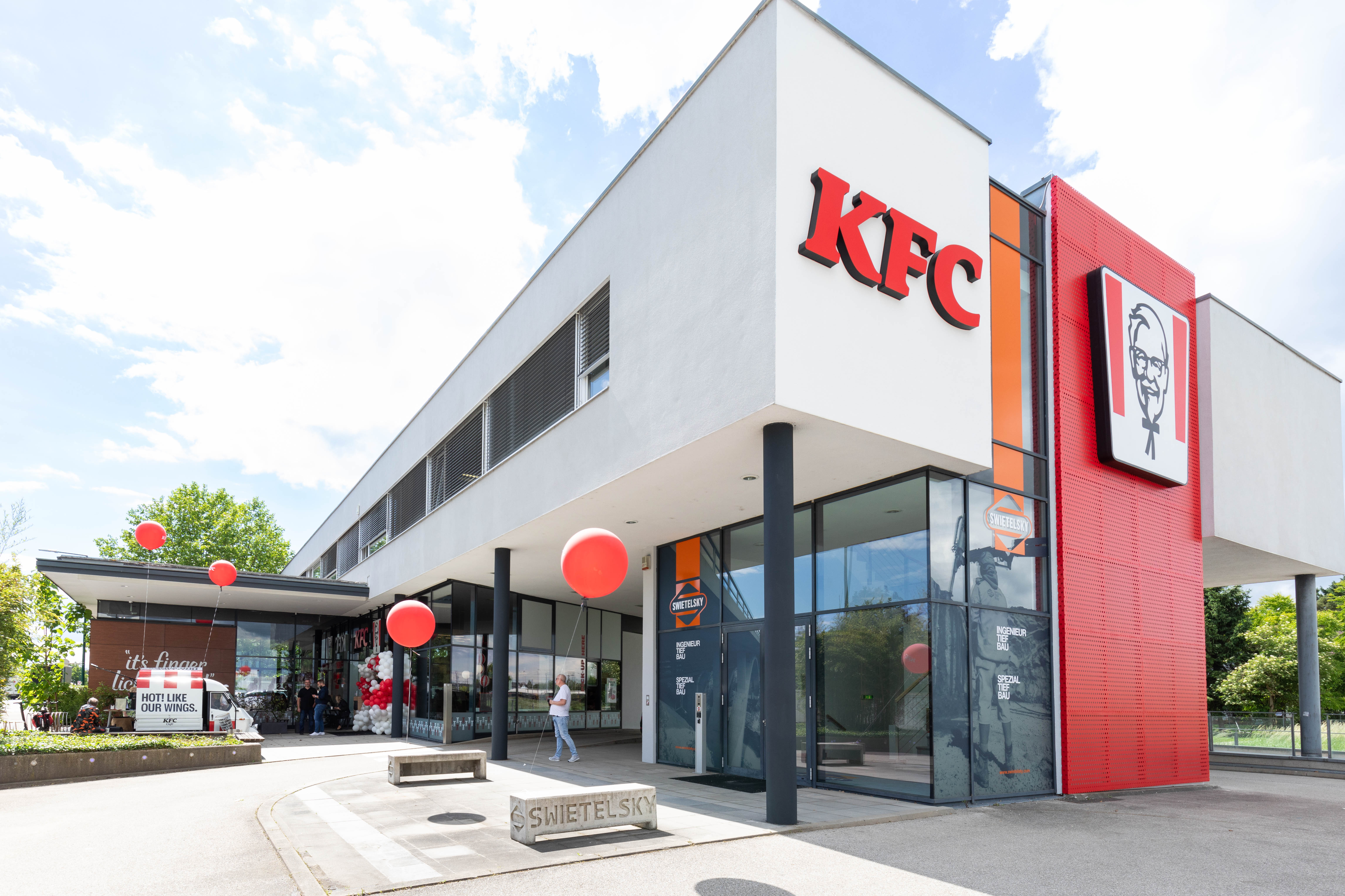 Fassade der KFC-Filiale Wels mit rotem Logo und roten Luftballons