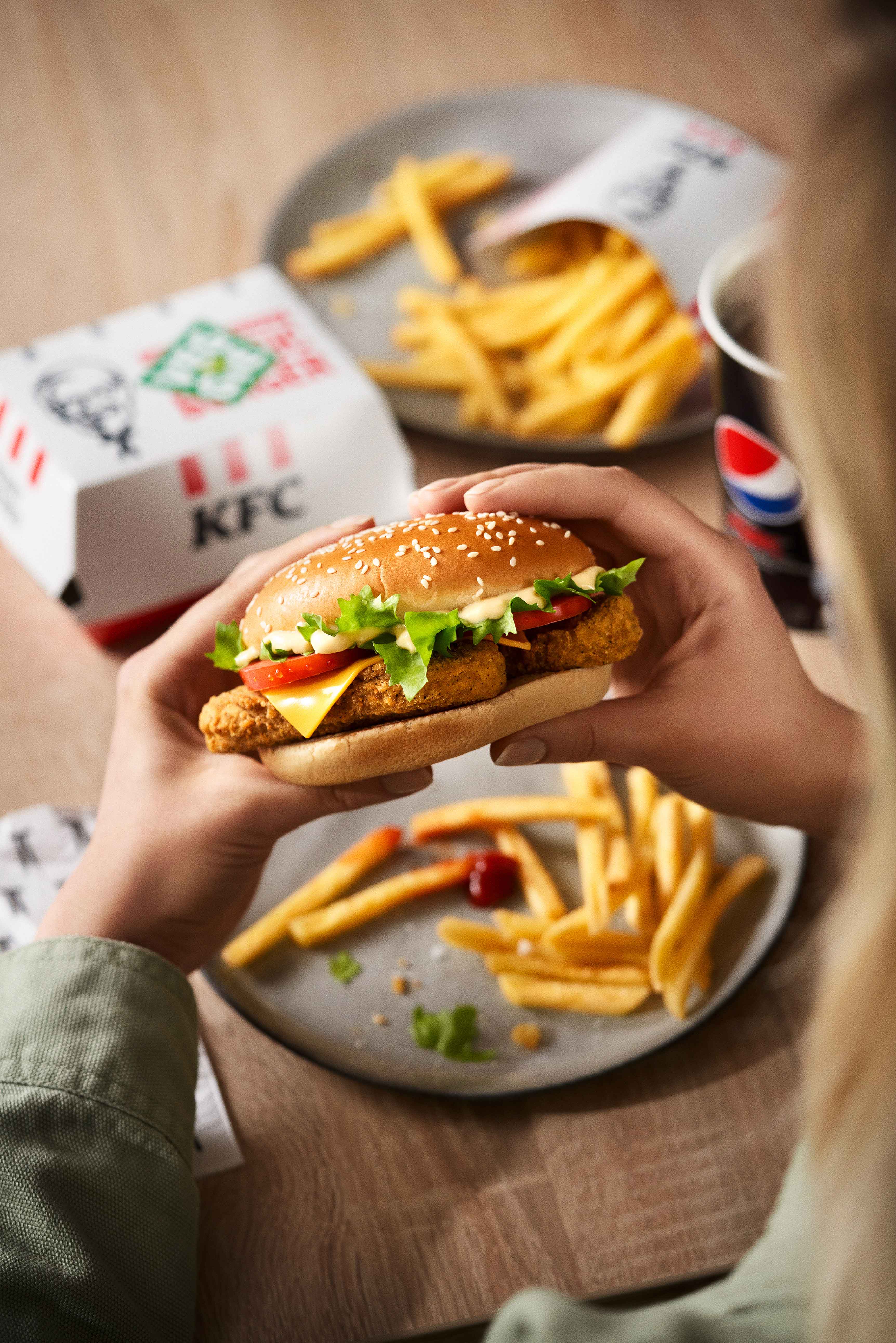 Hände halten KFC Veggie Burger, im Hintergrund Pommes und Cola