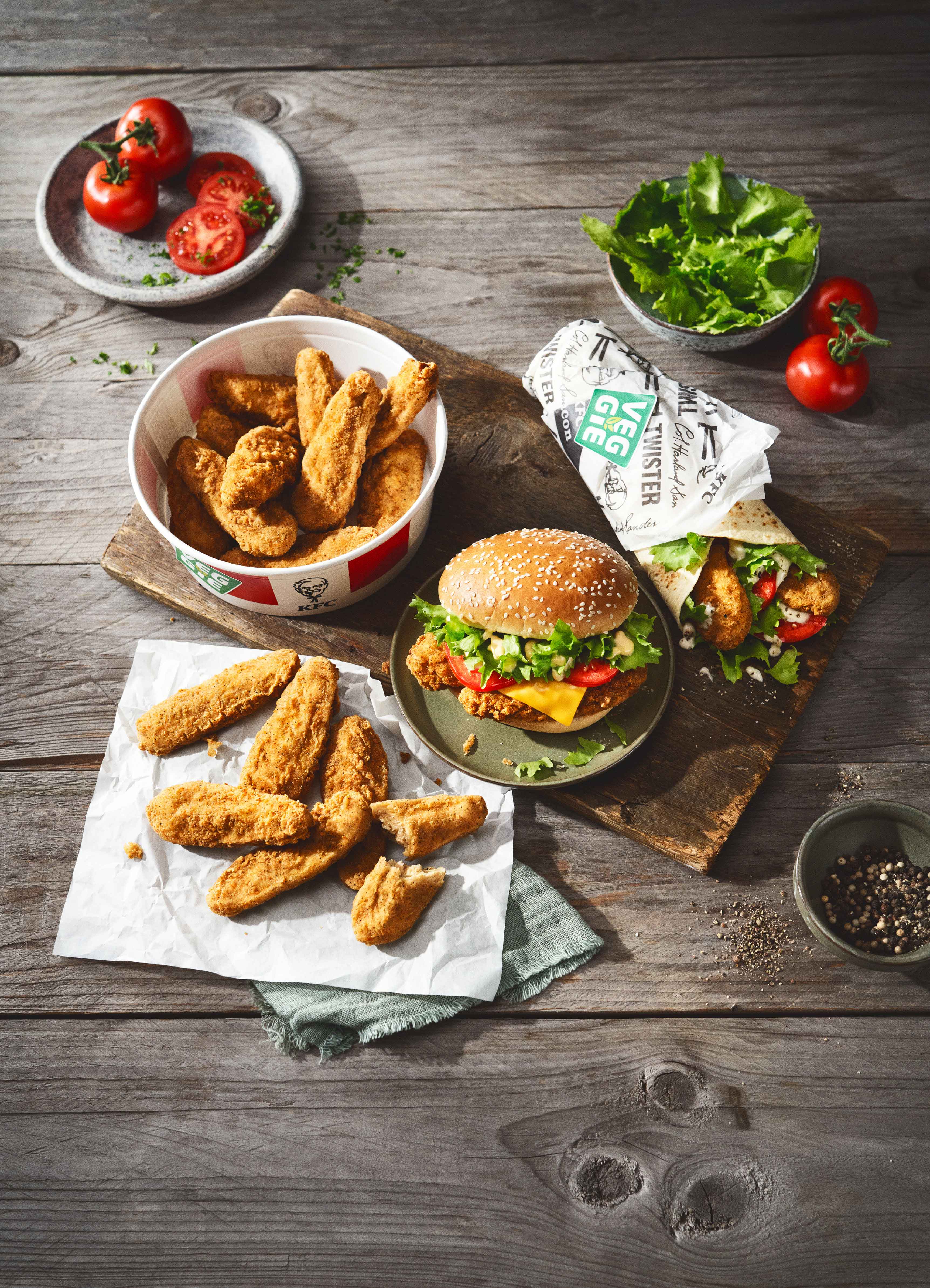 KFC-Veggie-Sortiment: Tenders, Burger, Wrap und Tomaten auf einem Tisch arrangiert